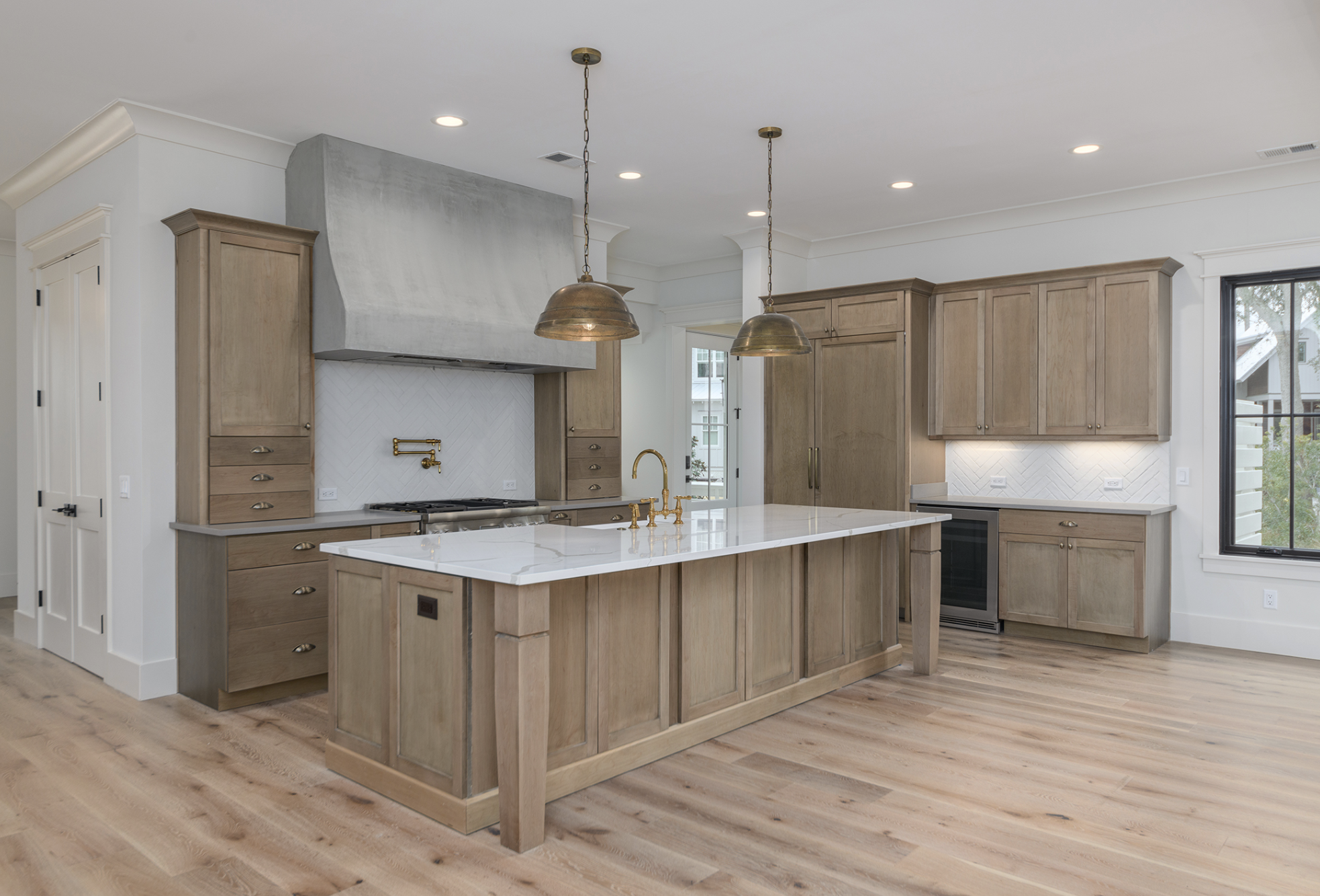 Modern kitchen with wooden cabinets, a white marble island, brass fixtures, a stainless steel stove, and large windows.
