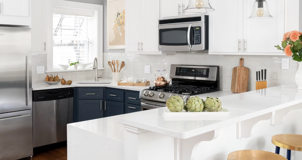 Modern kitchen with white cabinets, stainless steel appliances, a white countertop, a tray of artichokes, and a window with blinds.
