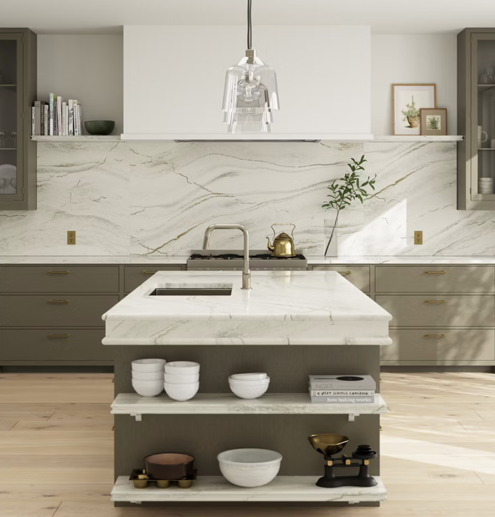 Modern kitchen with marble countertops, an island with a sink, and gray cabinetry. Features open shelves with bowls and books, a gold kettle, and minimalistic decor.