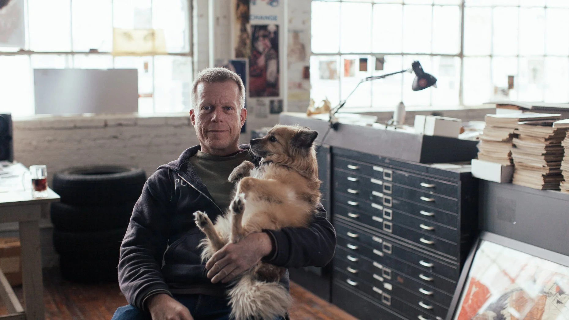 Derek Hess sits in his studio with his dog Rommel