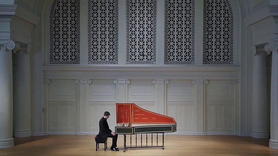 Jason Moy sitting in front of his Harpsichord in a music hall