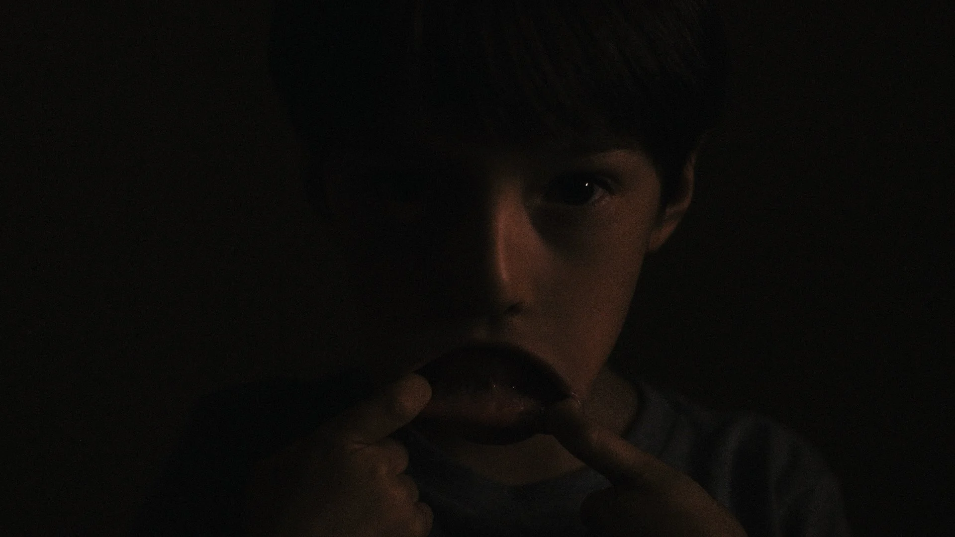 Still of dimly lit kid making weird face