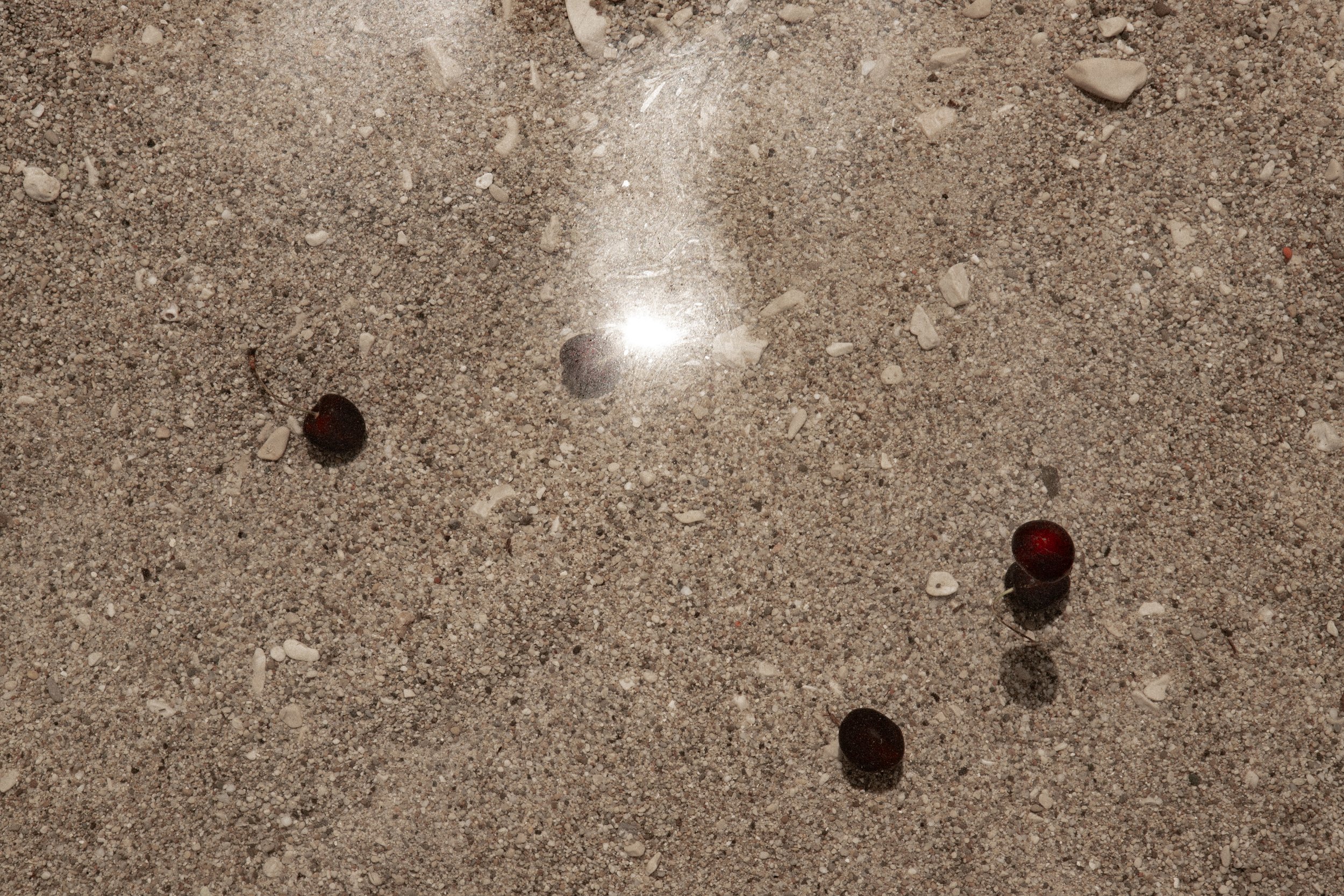 Photographie estivale prise sur les îles du Frioul de cerises bien mûres qui flottent dans l'eau. En fond on voit le sable dans la mer Méditerranée et le reflet du soleil de l'été marseillais
