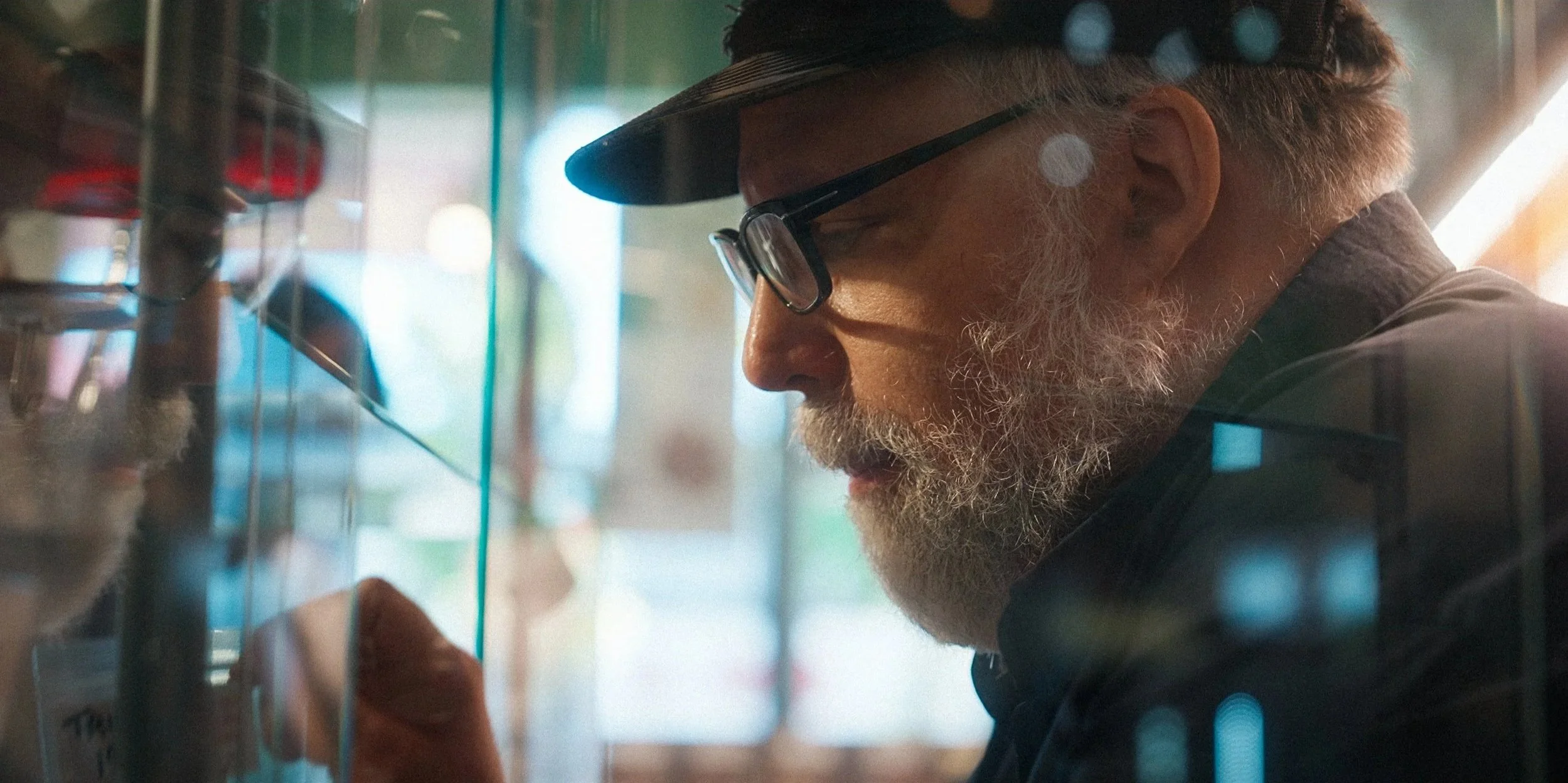 David Malmo-Levine, a Vancouver-based drug activist and manager at the Coca Leaf Cafe is shown wearing a cap, examining psychedelics through a glass display case in the Coca Leaf Cafe.
