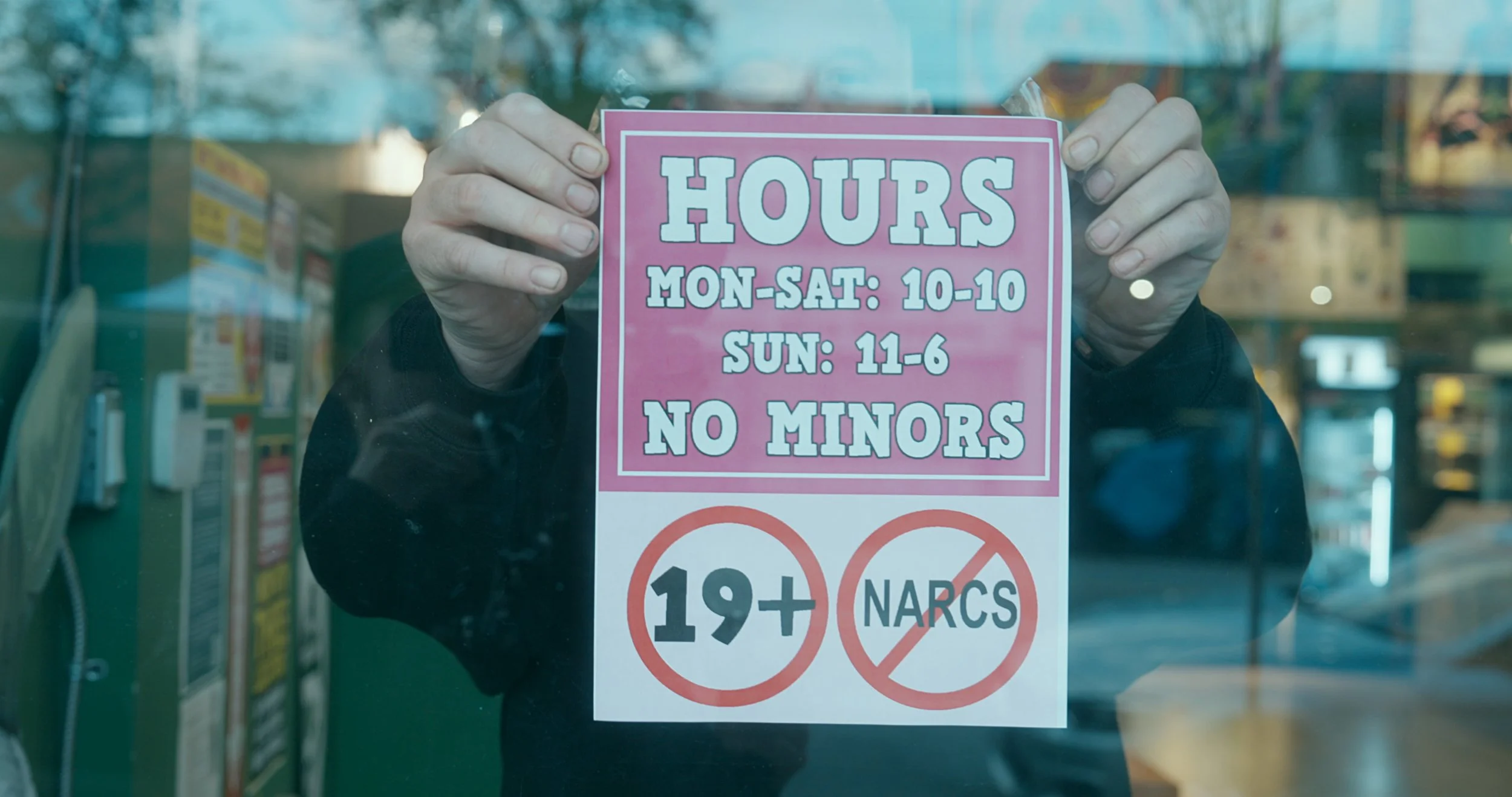 Dana Larsen, a prominent Canadian drug activist, is showing a holding a pink Coca Leaf Cafe sign with their business hours and age restrictions on their store front.