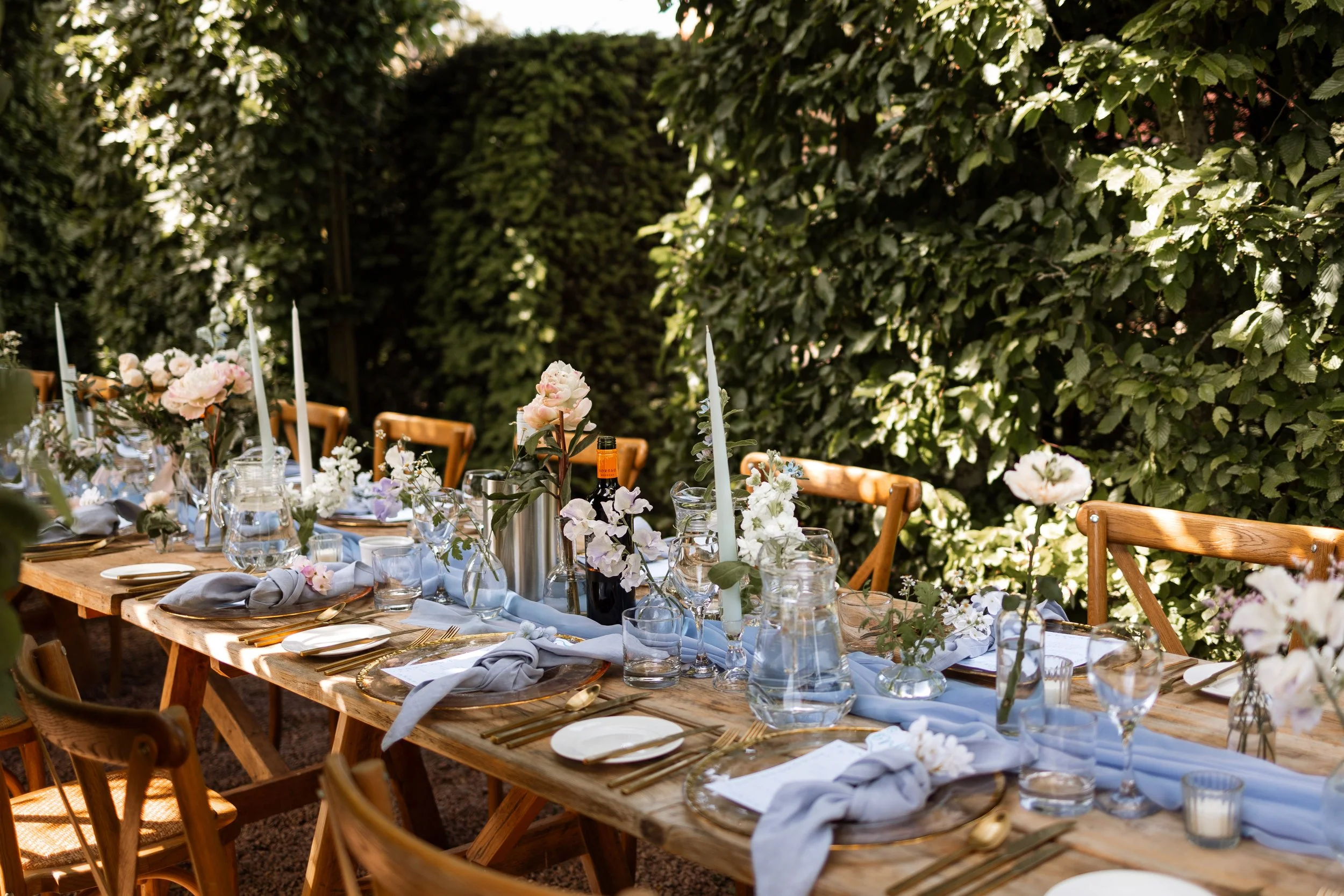 beautiful garden dinner table. set with long candles, billowing flowers, and glassware.