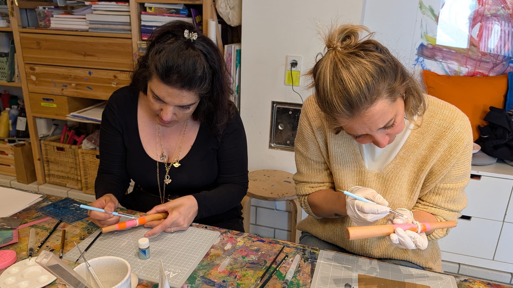Zwei Frauen arbeiten in einem Kreativstudio mit DIY-Werkzeugen und Farben an Holzprojekten.