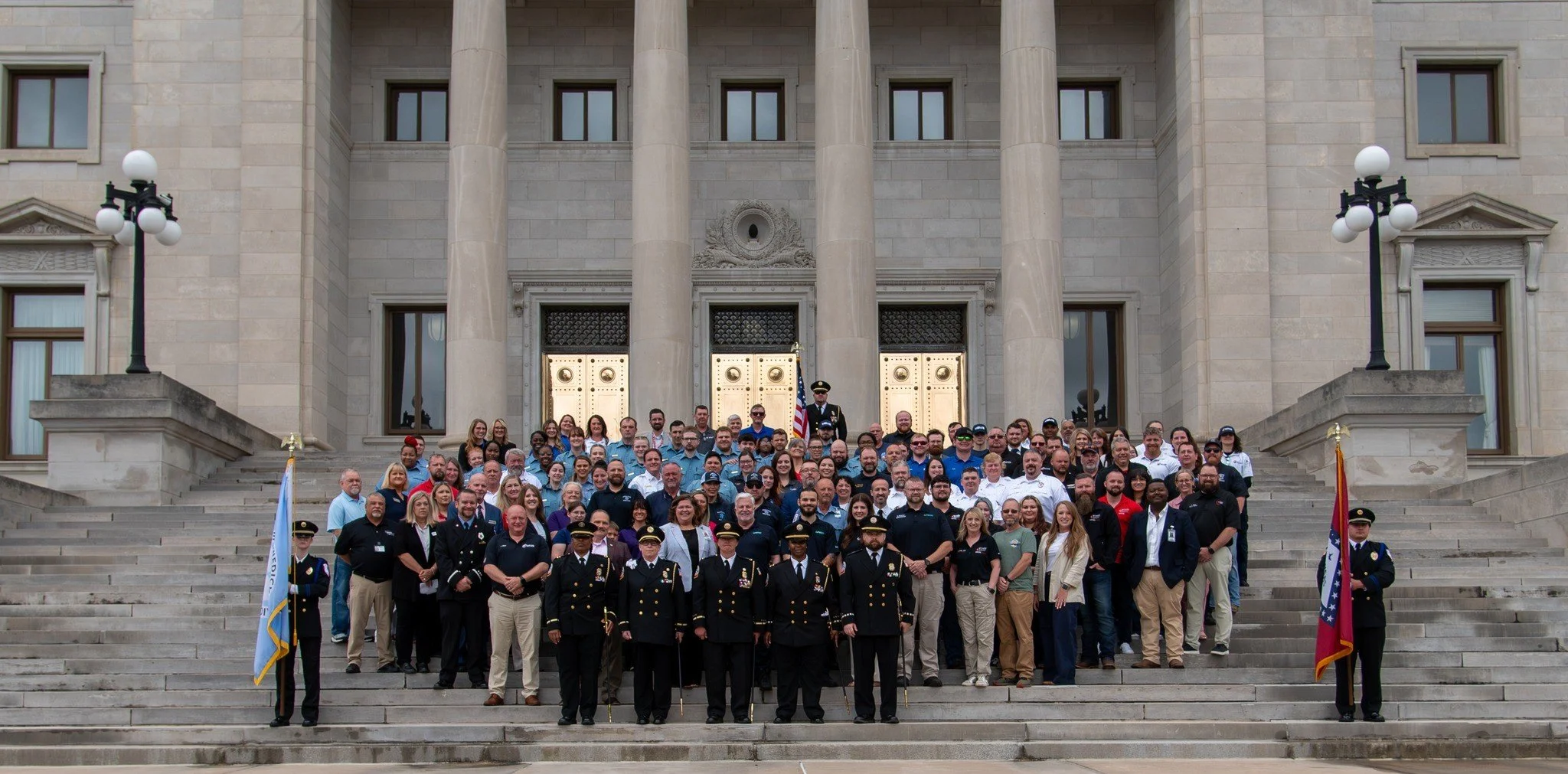 A large group of people standing on the steps of a government building with tall stone columns, some people in uniform, posing for a photo.