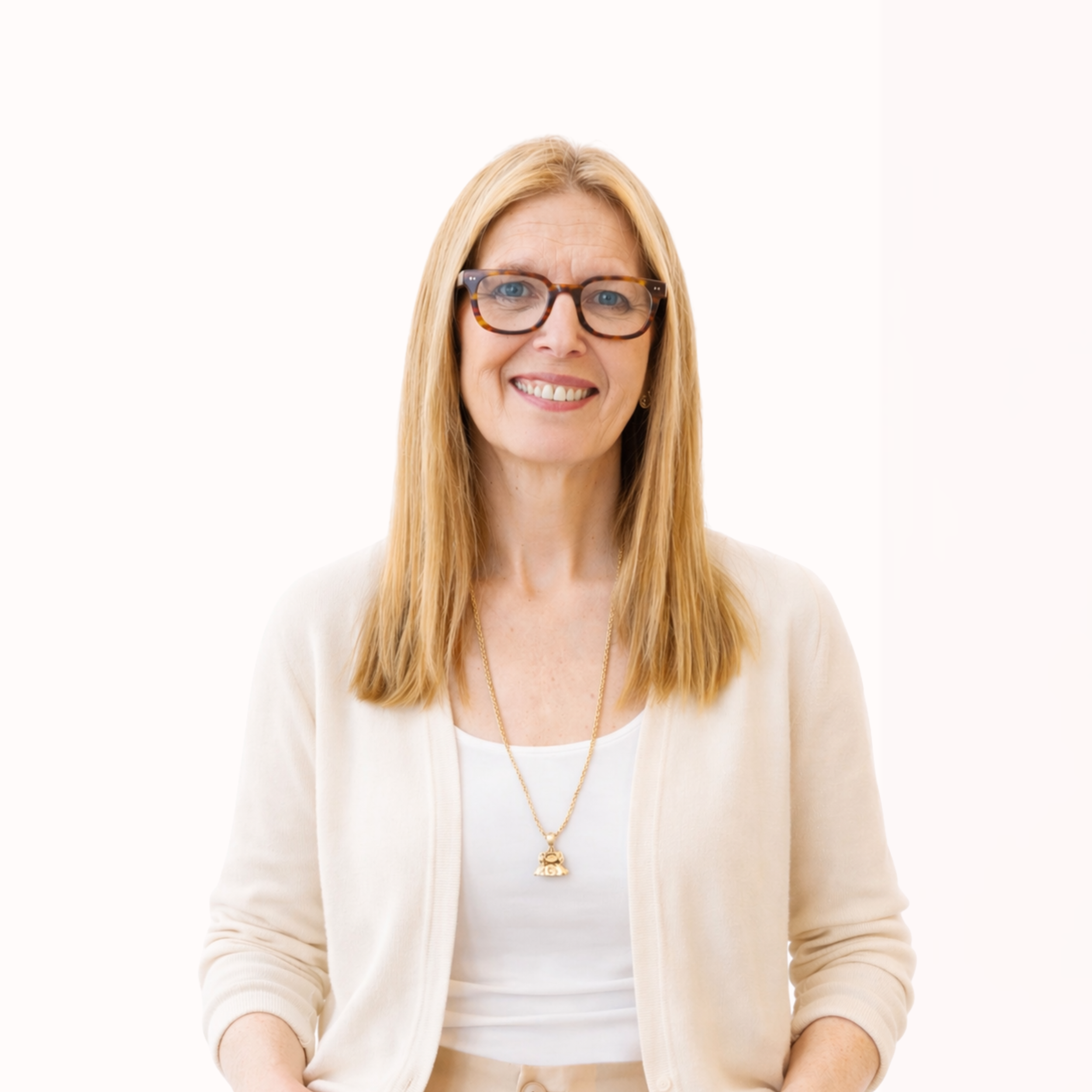 A smiling woman with long blonde hair wearing tortoiseshell glasses, a white top, beige cardigan, and a gold necklace with a pendant, standing against a plain white background.