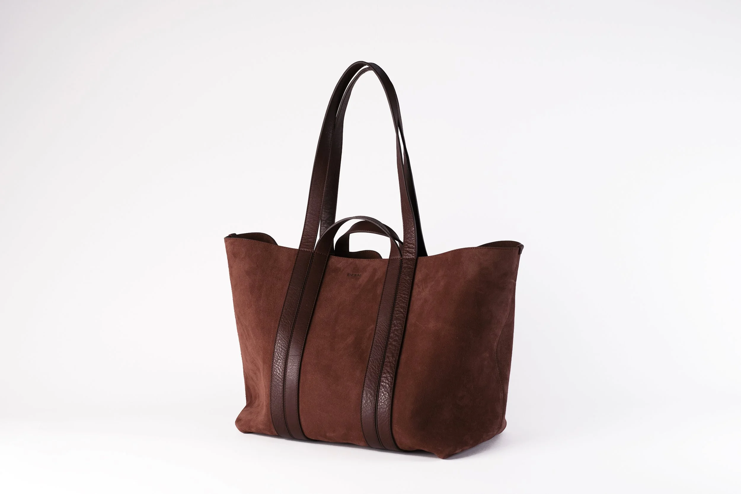 A large brown tote bag made of suede with leather handles and trim, placed against a plain white background.