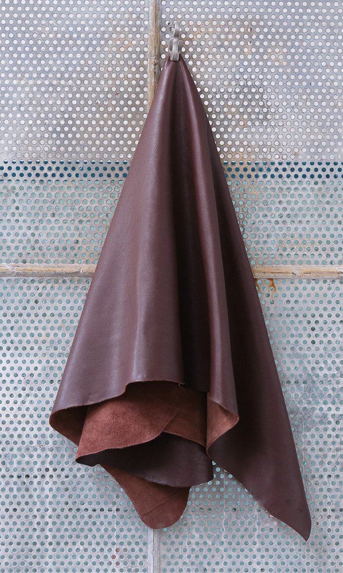 A coat or fabric piece hanging on a hook against a perforated metallic wall.
