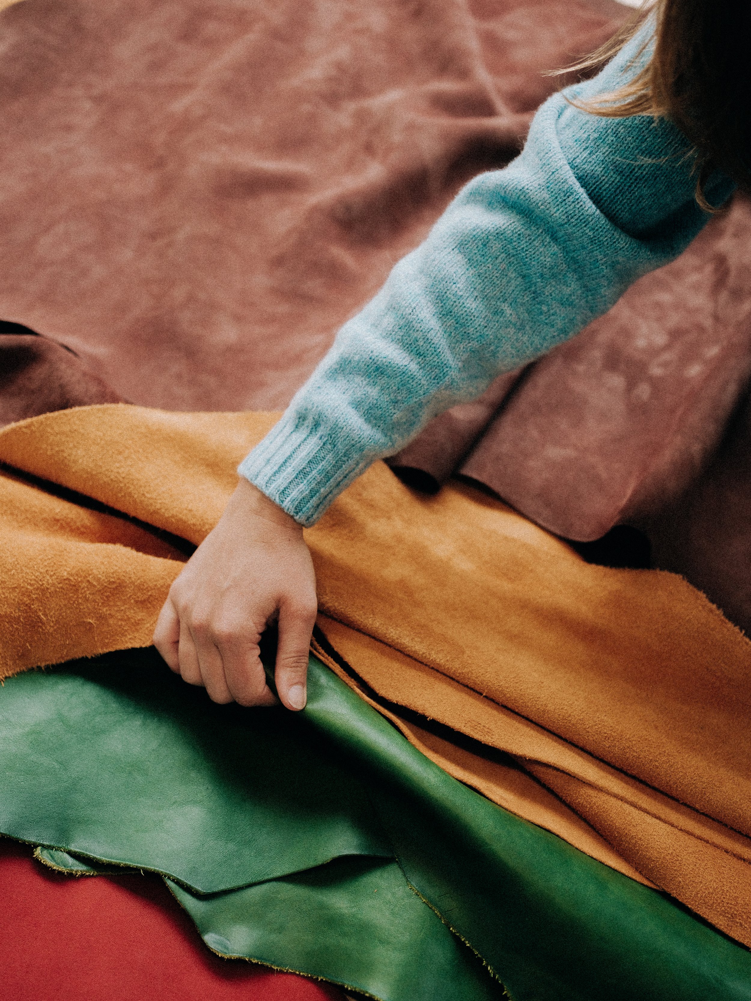 Close-up of a person's hand resting on layered fabric in green, orange, and pink colors, with a light blue long-sleeve shirt sleeve visible.