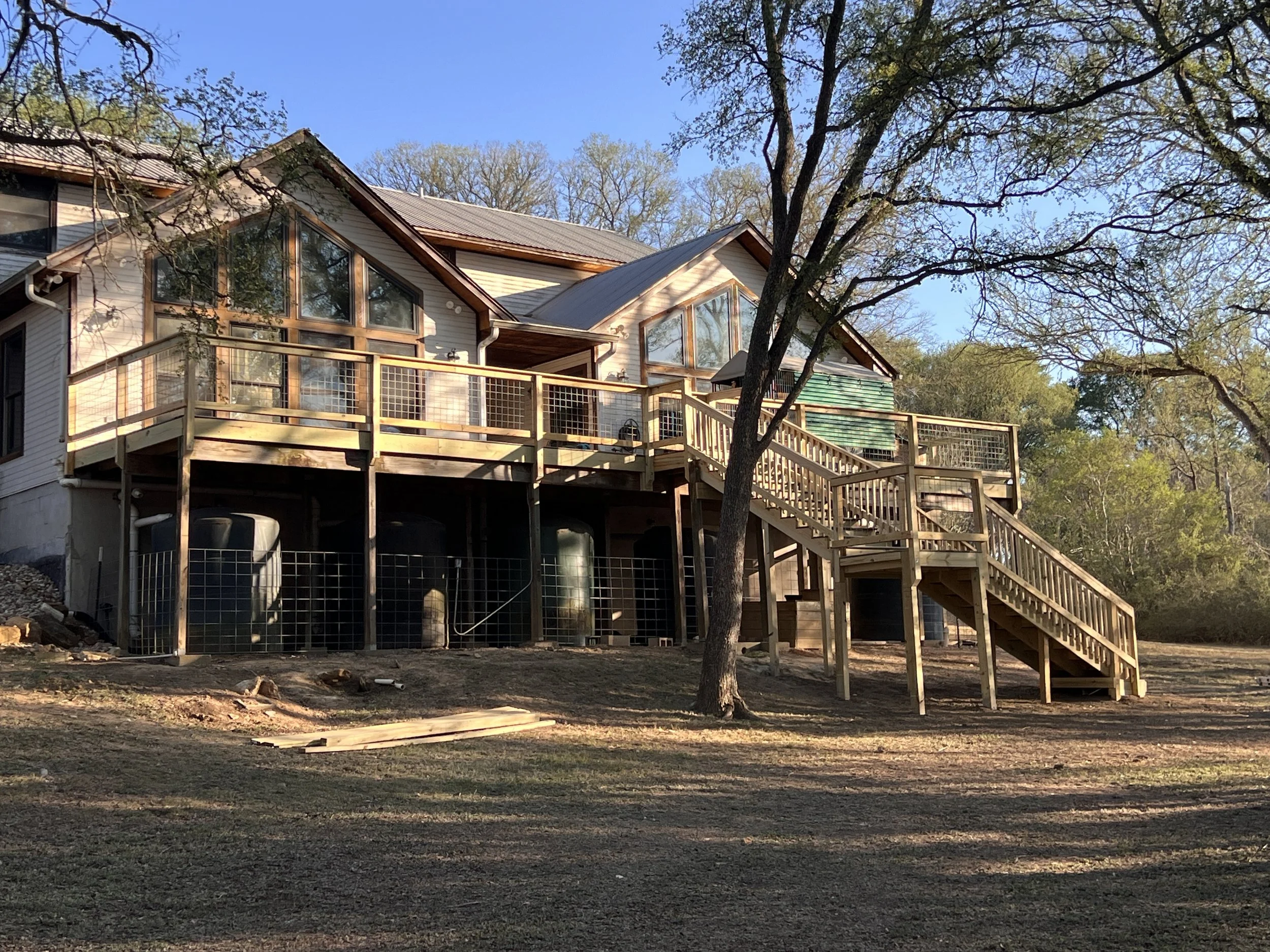 A multi-level house with a wooden deck and stairs, situated on a grassy area with trees in the background.