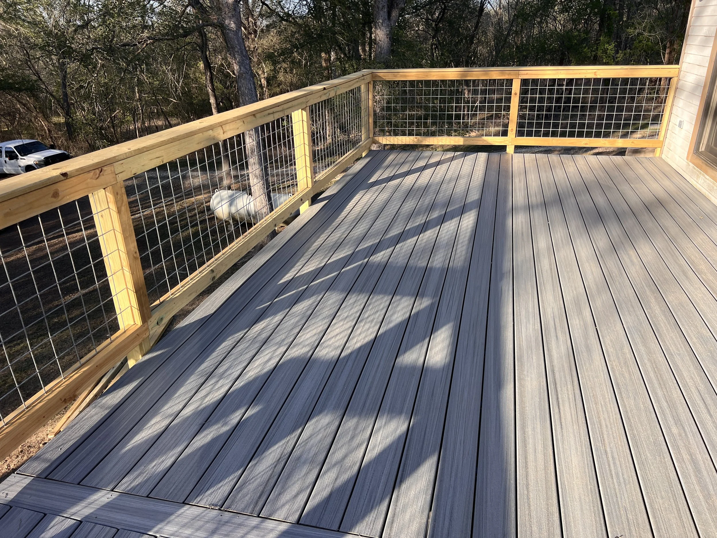 Newly built wooden deck with safety railings overlooking a wooded area with trees and a white object.