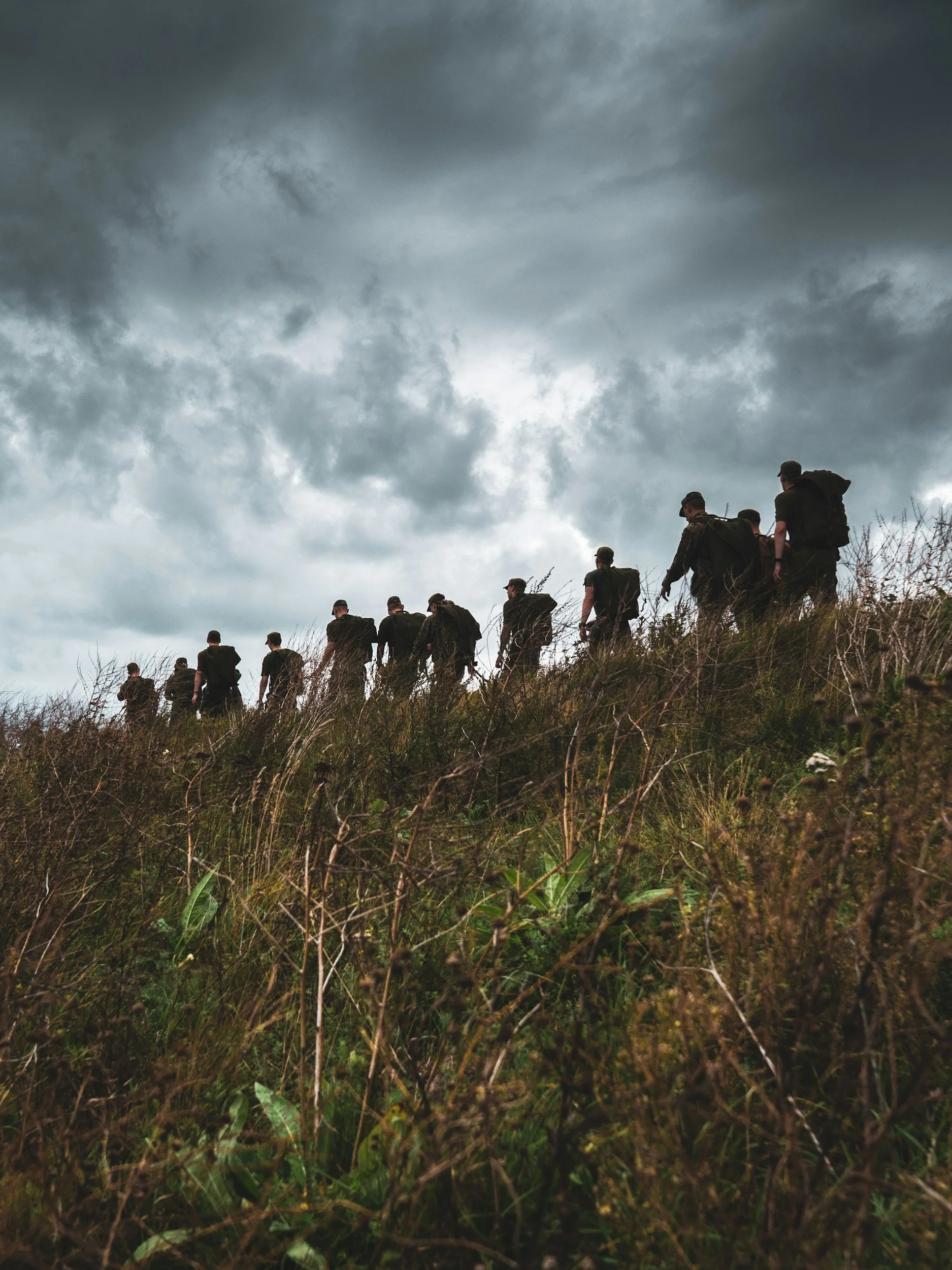 A troop of soldiers walking down a hill on an overcast day.