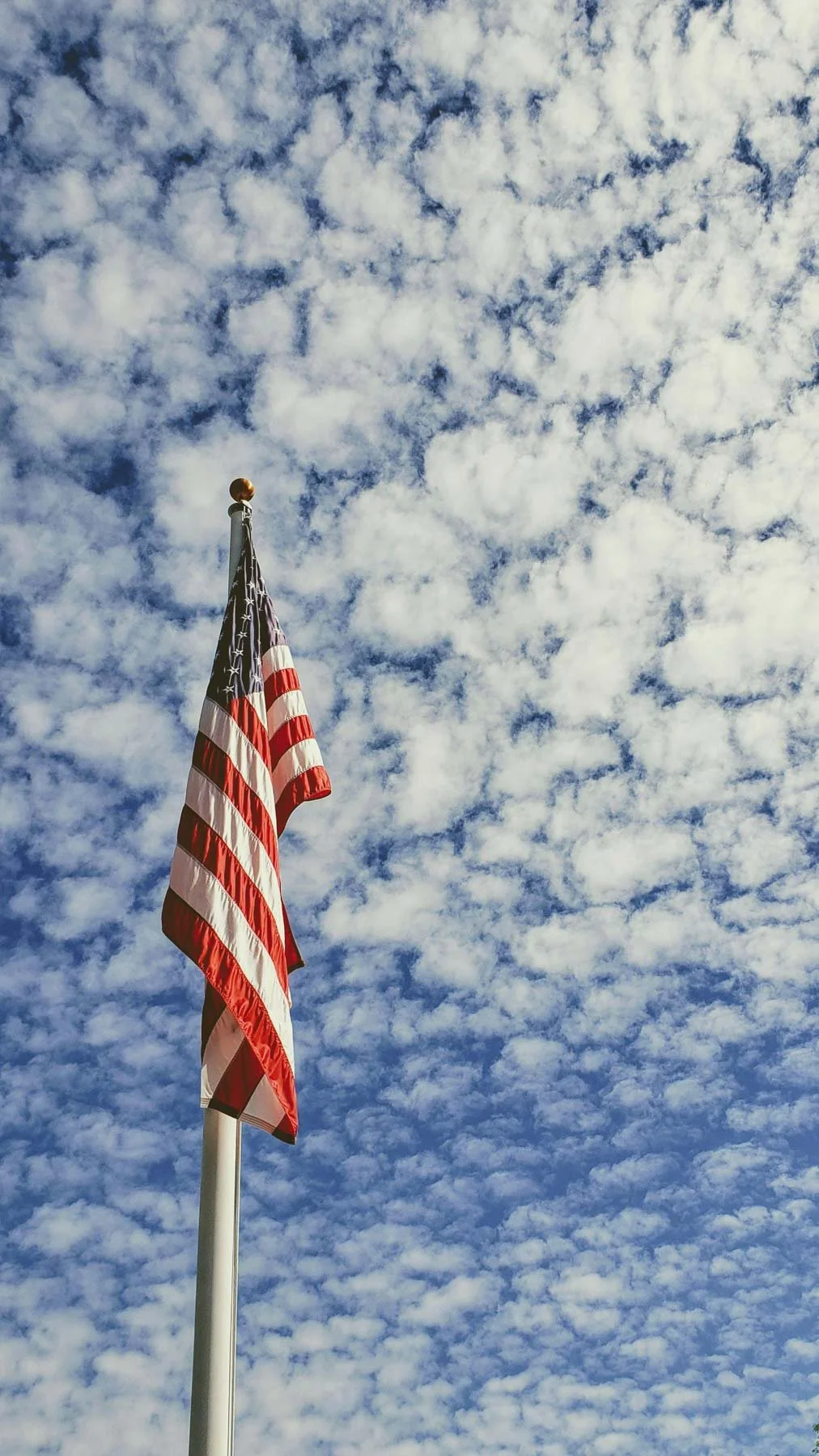 American flag flying on a flagpole against a cloudy sky.