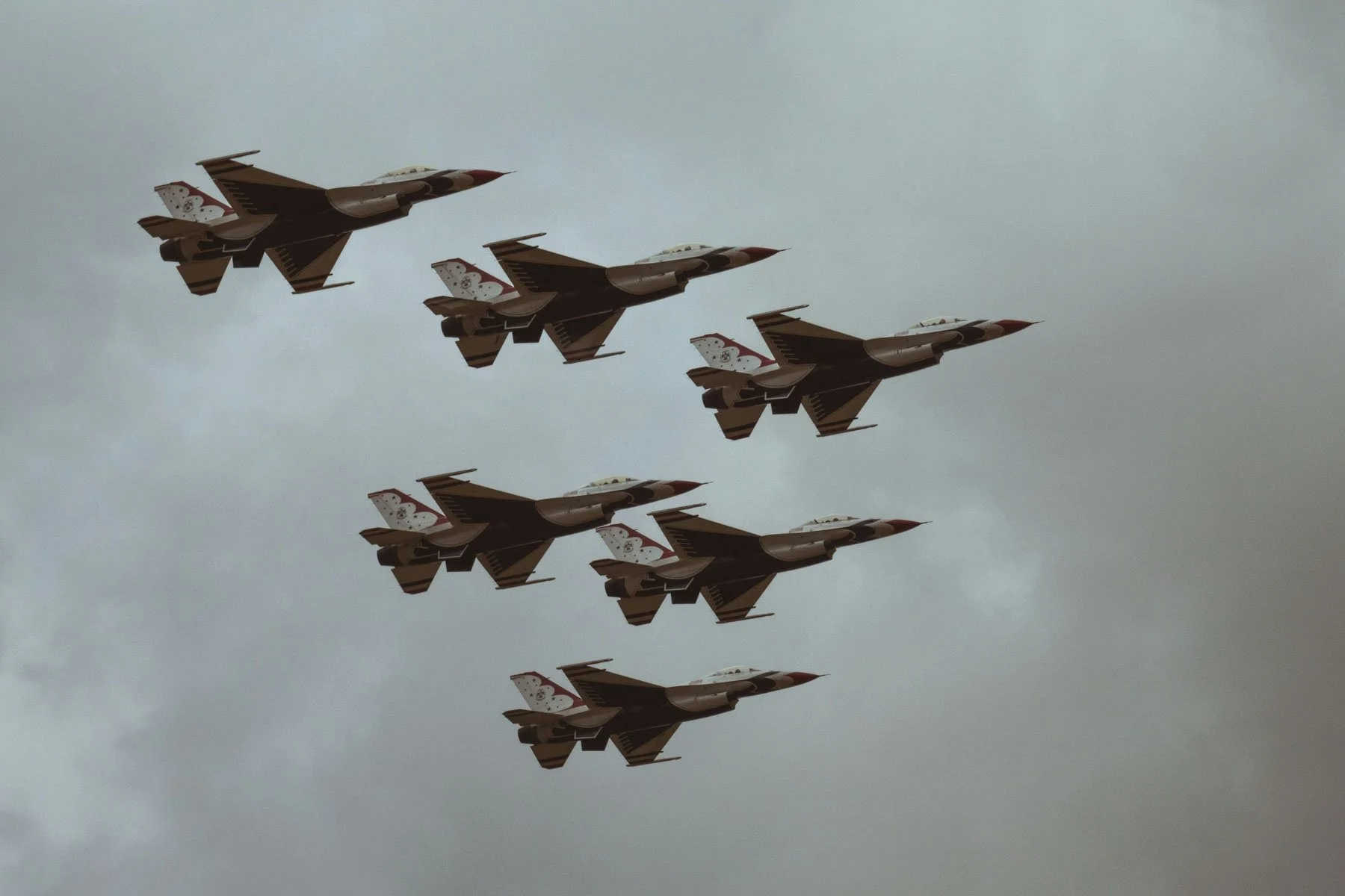 Six fighter jets flying in formation against a cloudy sky.