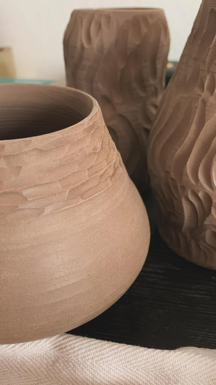 Vasi di ceramica non smaltata con superfici ruvide e dettagli scolpiti, in tonalità di marrone chiaro e scuro.