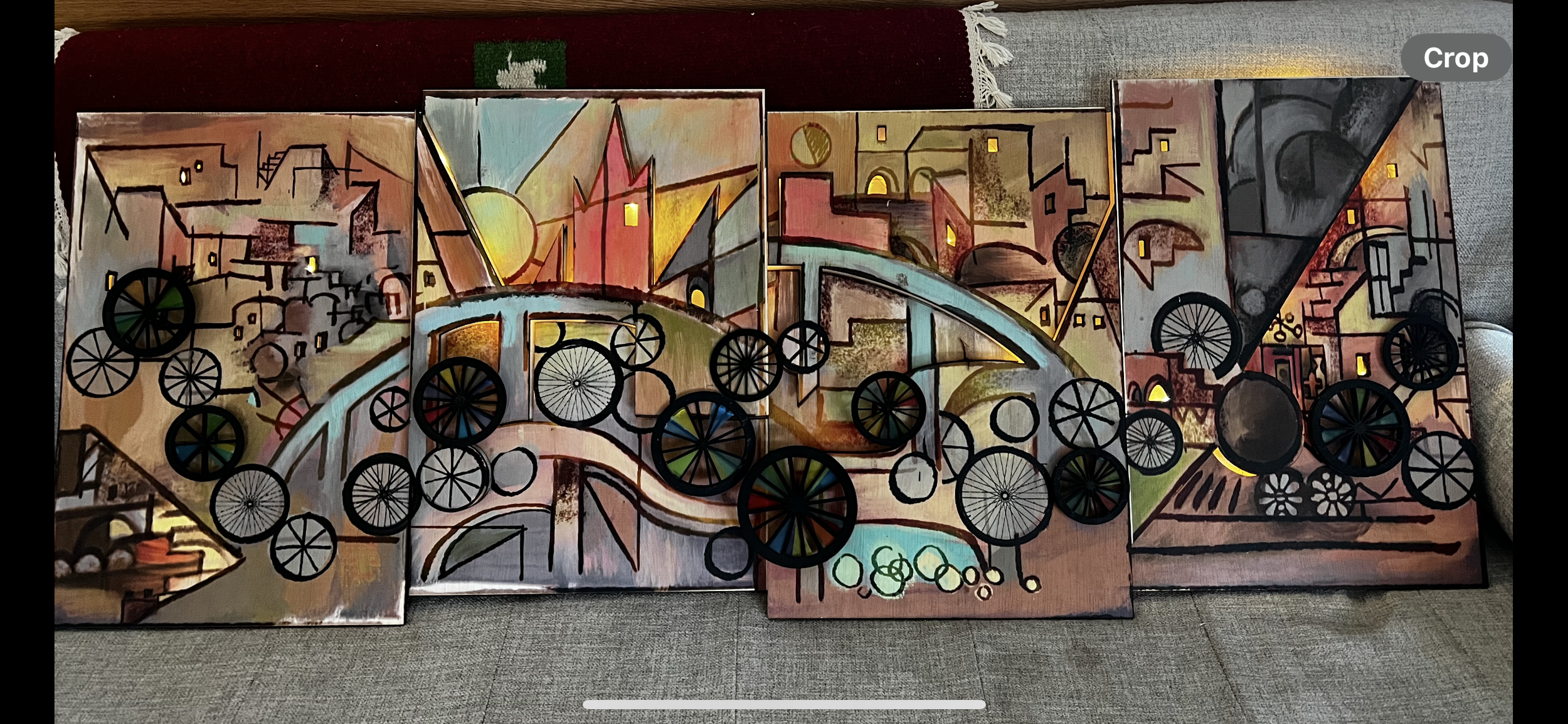A colorful abstract painting with geometric shapes, cityscape elements, and bicycle wheel motifs on a multi-panel canvas.