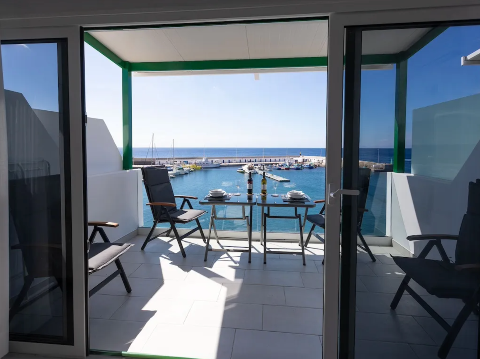 Balcony with a table set for dinner overlooking a marina with boats and the ocean in the background.