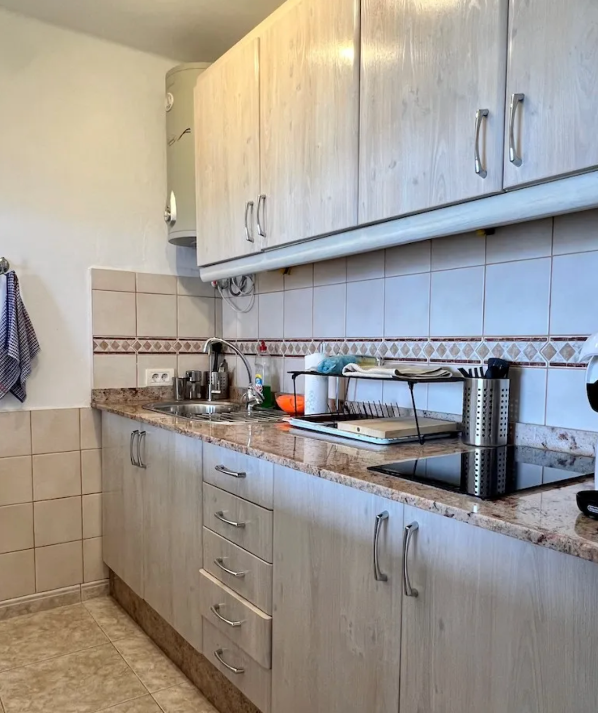 Kitchen with beige cabinets, tile backsplash, countertop with sink, dish rack, and small appliances.
