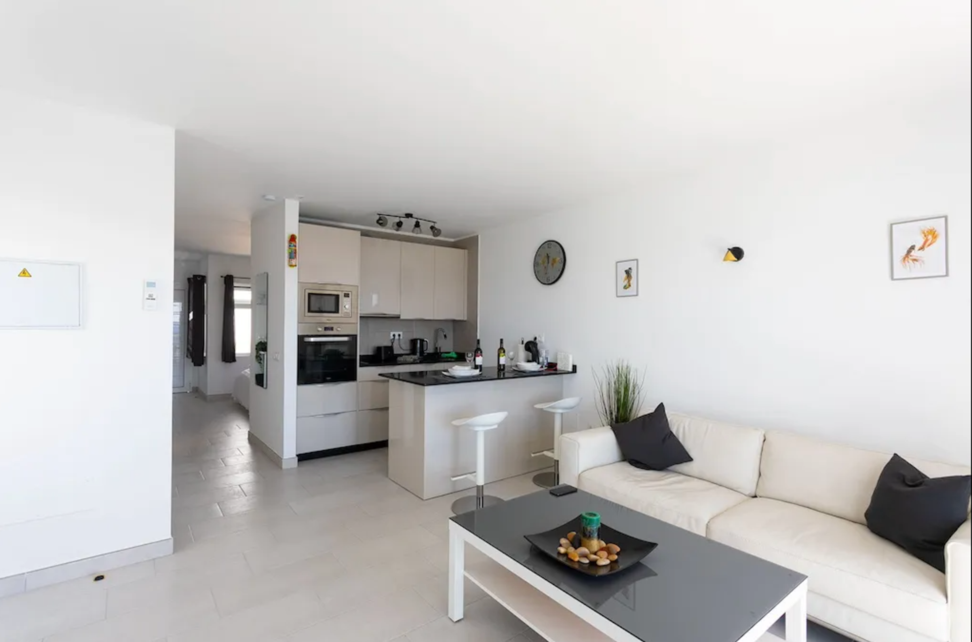 Open-concept living room and kitchen with white walls, black accents, and modern furniture in a bright apartment.