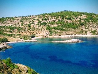 Scenic view of a body of water with land and hills in the background under a clear blue sky. From Dr. Michael Kellis's village in Greece.