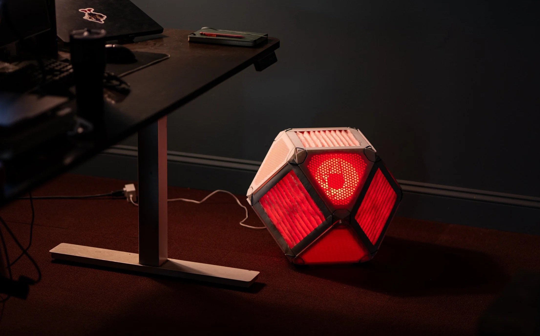 Glowing red OdddCube air purifier on the floor under a desk