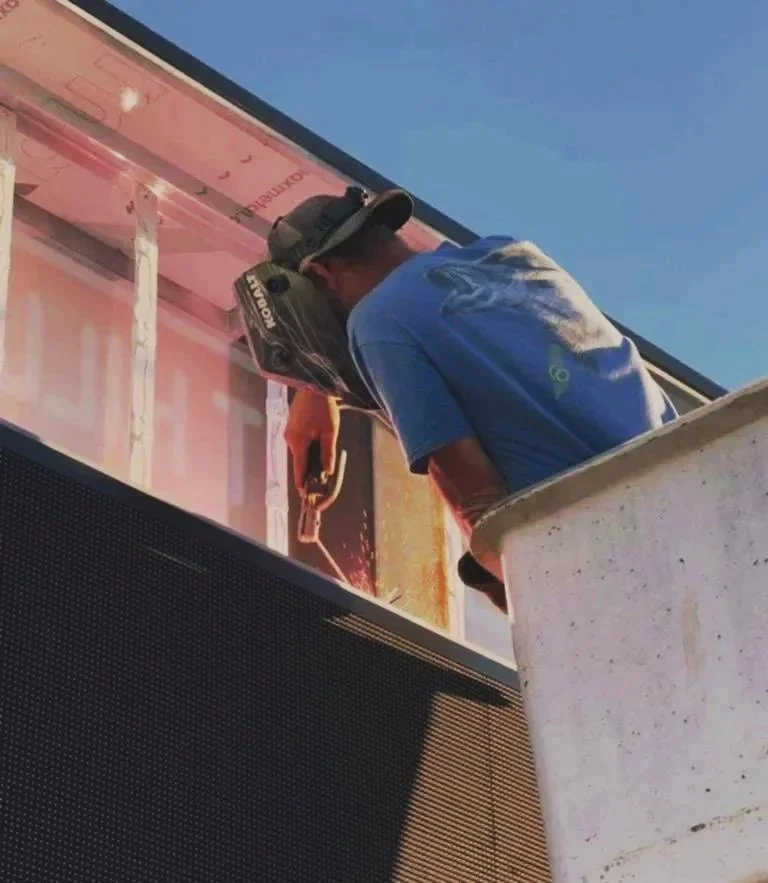 A construction worker using a power tool on a building's exterior wall during daytime.