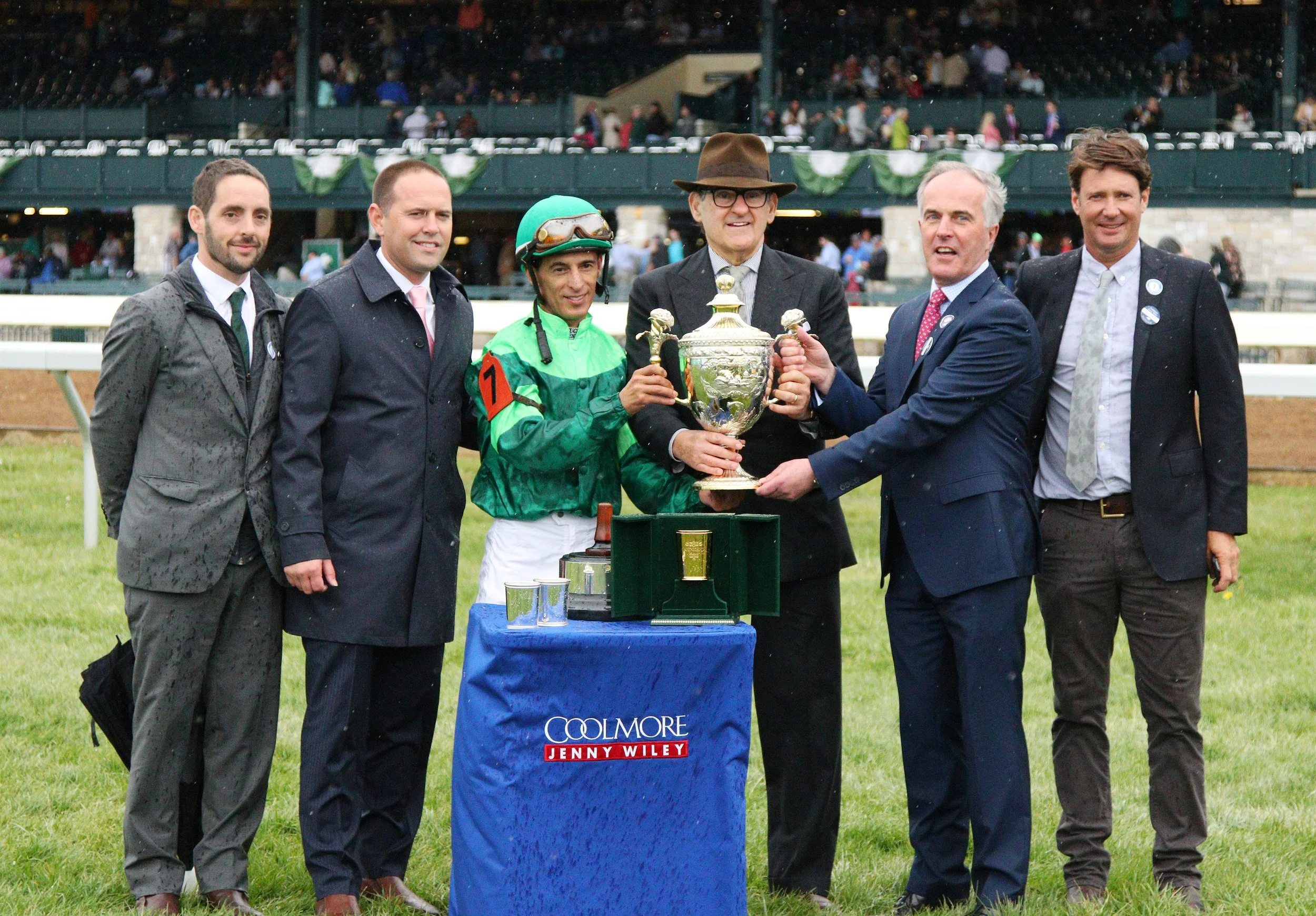 Racehorse owners, jockey, and team celebrating with a trophy in the winner’s circle, representing full racehorse ownership