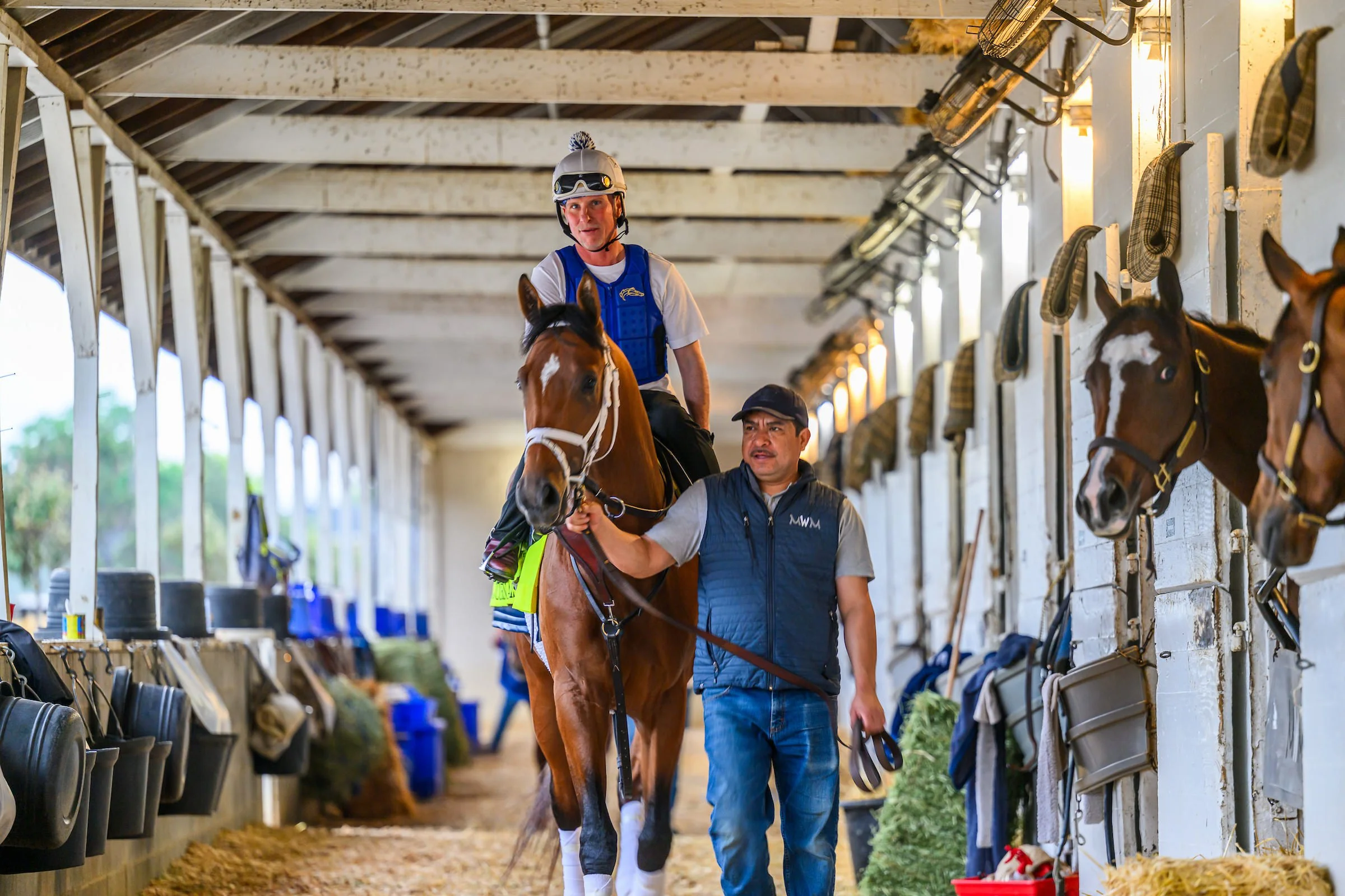 Racehorse being led through a stable with jockey aboard, showing the behind-the-scenes experience of getting started in racehorse ownership