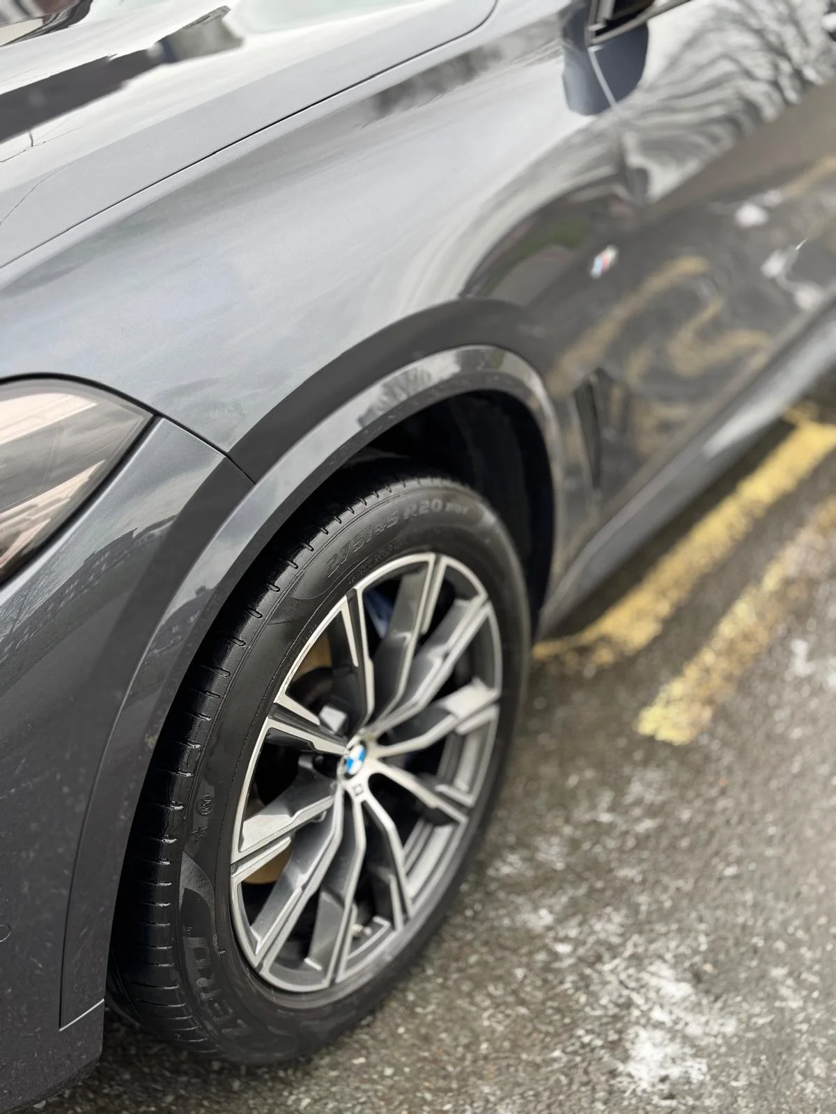 Close-up of a gray BMW car parked on a street, focusing on the front tire and wheel with a black and silver design.