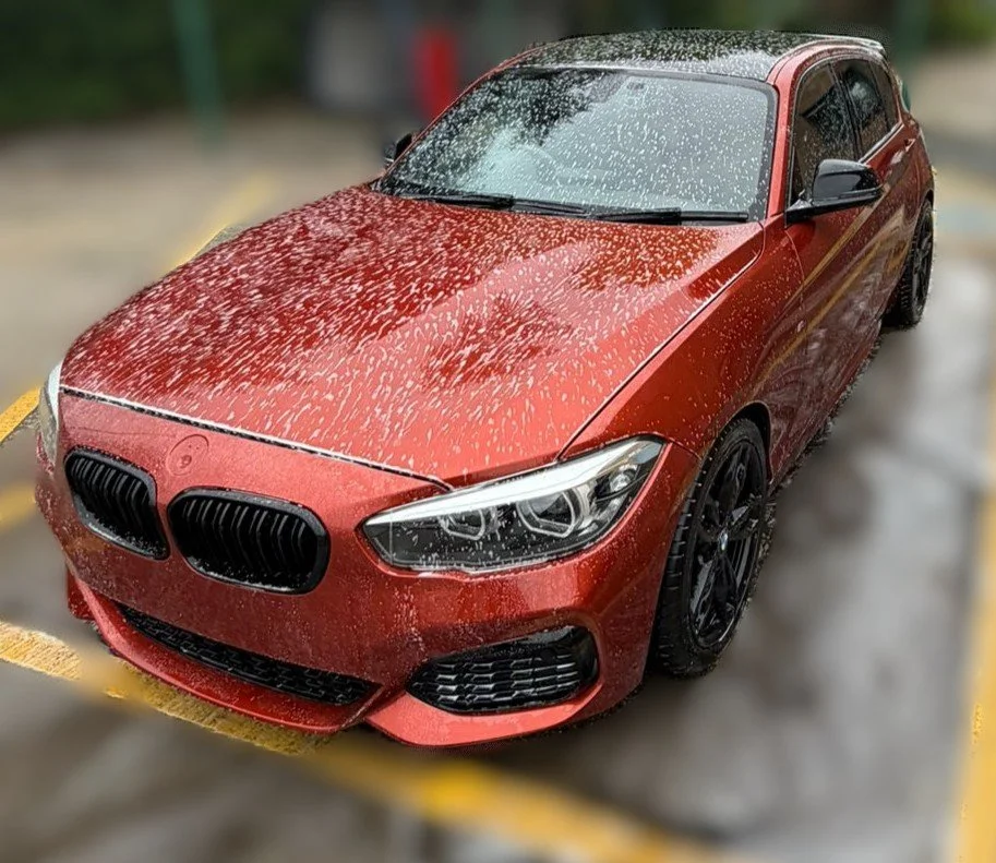 Red BMW car with water droplets on it, parked in a wet parking lot.