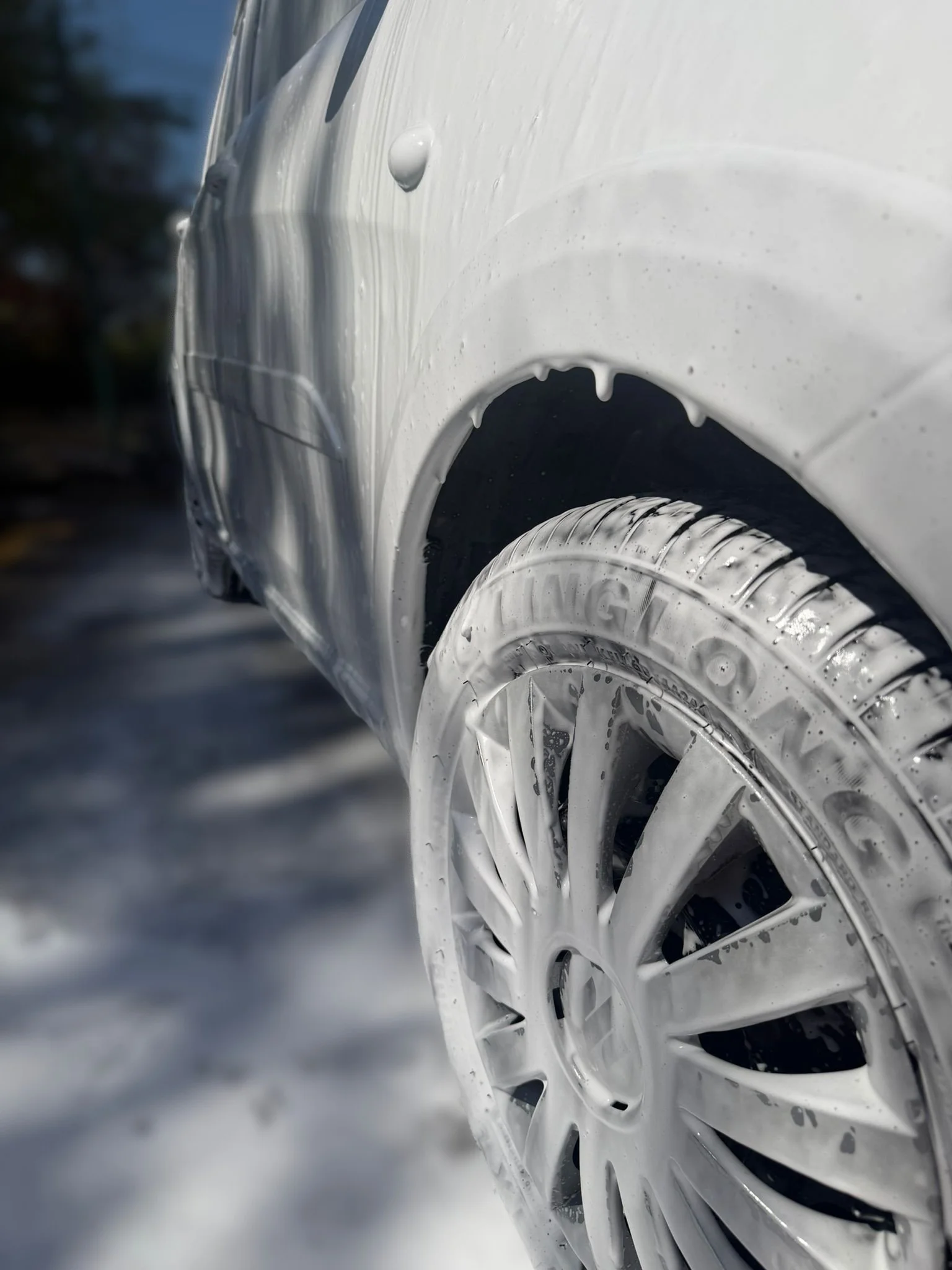 Close-up of a white car wheel covered in soap suds with a blurred background.