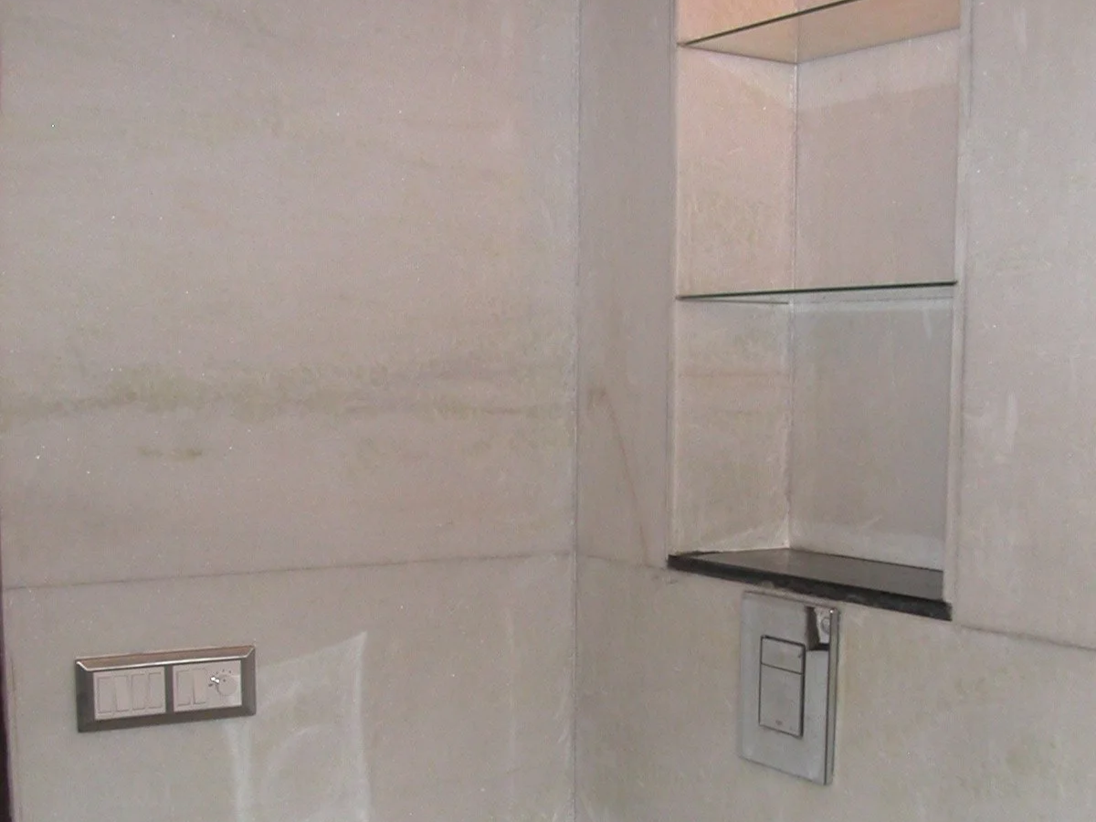 Close-up of a beige tiled wall with built-in shelves, a switch panel, and a flush button.