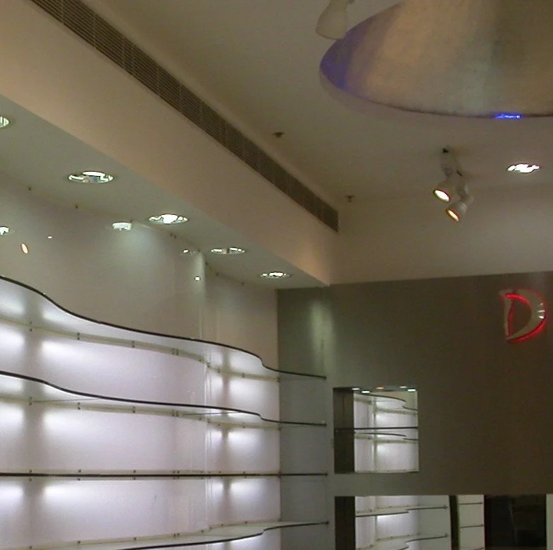 Interior of a modern building with curved white wall panels, ceiling lights, and a partial view of the letter D in red, possibly part of a sign or logo.