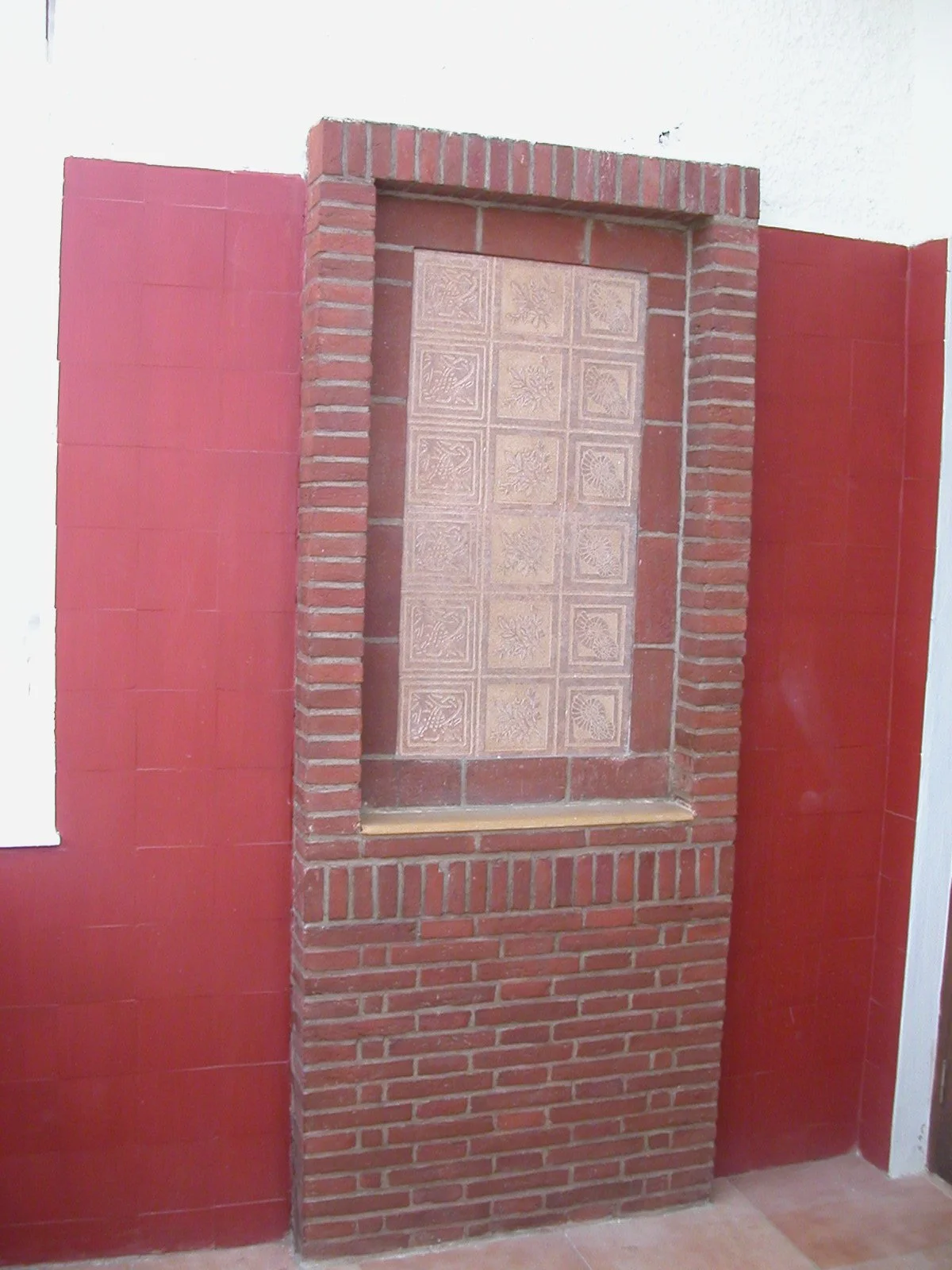 A decorative brick fireplace with a tiled interior, surrounded by red wall tiles and a white wall in the background.