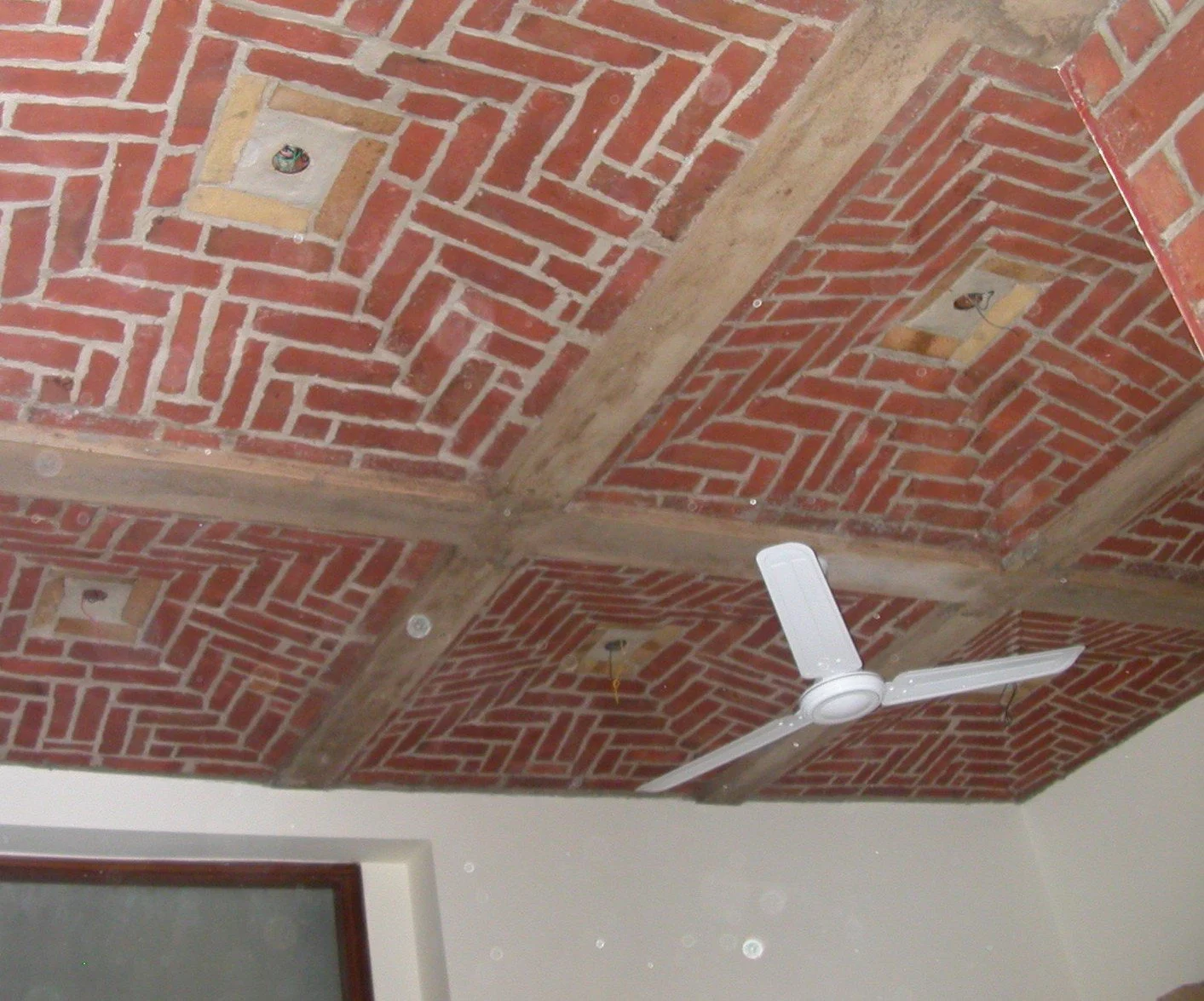 Ceiling with exposed red brick and wooden beams, white ceiling fan, recessed lighting fixtures, and a portion of a door with frosted glass.