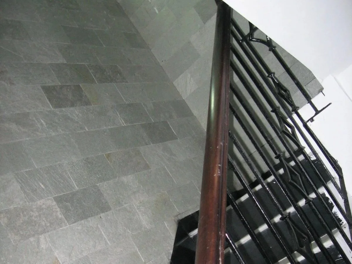 A staircase with black metal railing and a wooden handrail adjacent to a gray tiled floor.