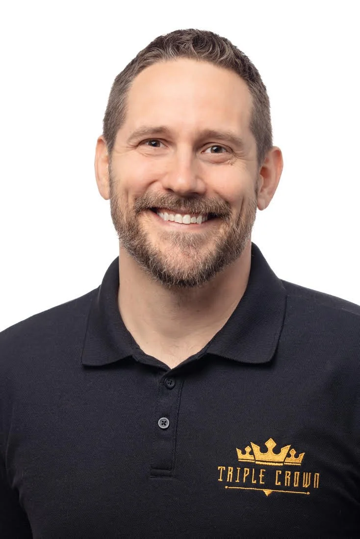 Smiling man with short hair and beard wearing a black polo shirt with a gold "Triple Crown" logo.