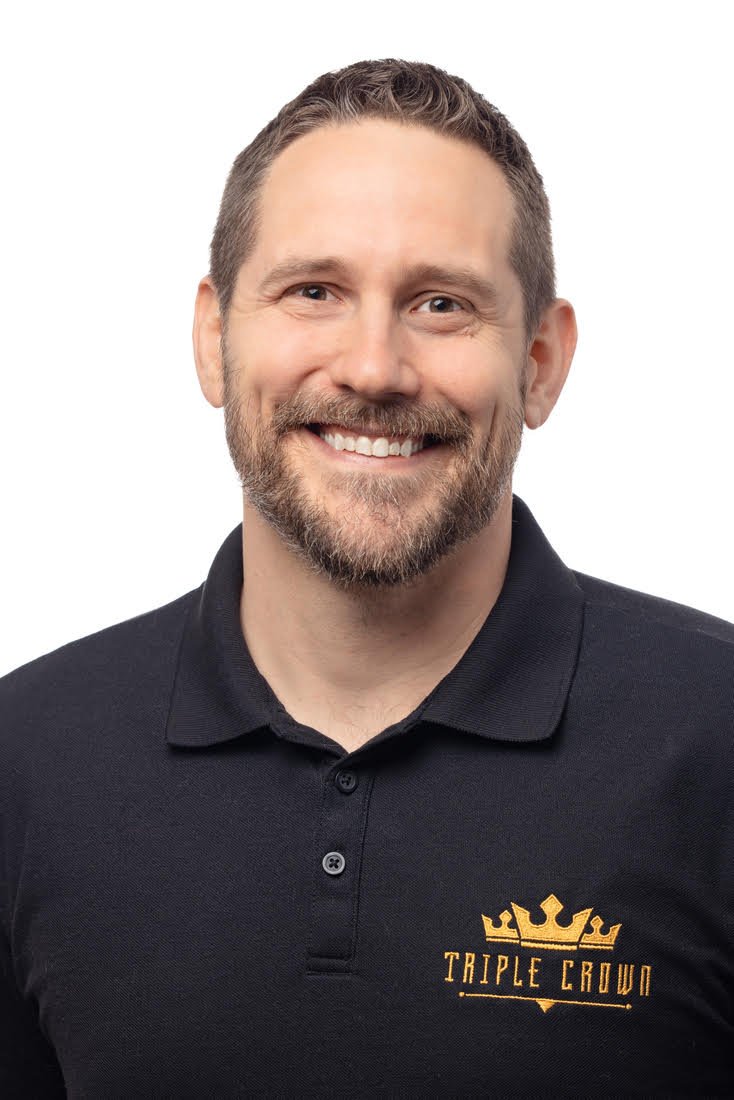 Man in black polo shirt with logo reading "Triple Crown" smiling against white background.