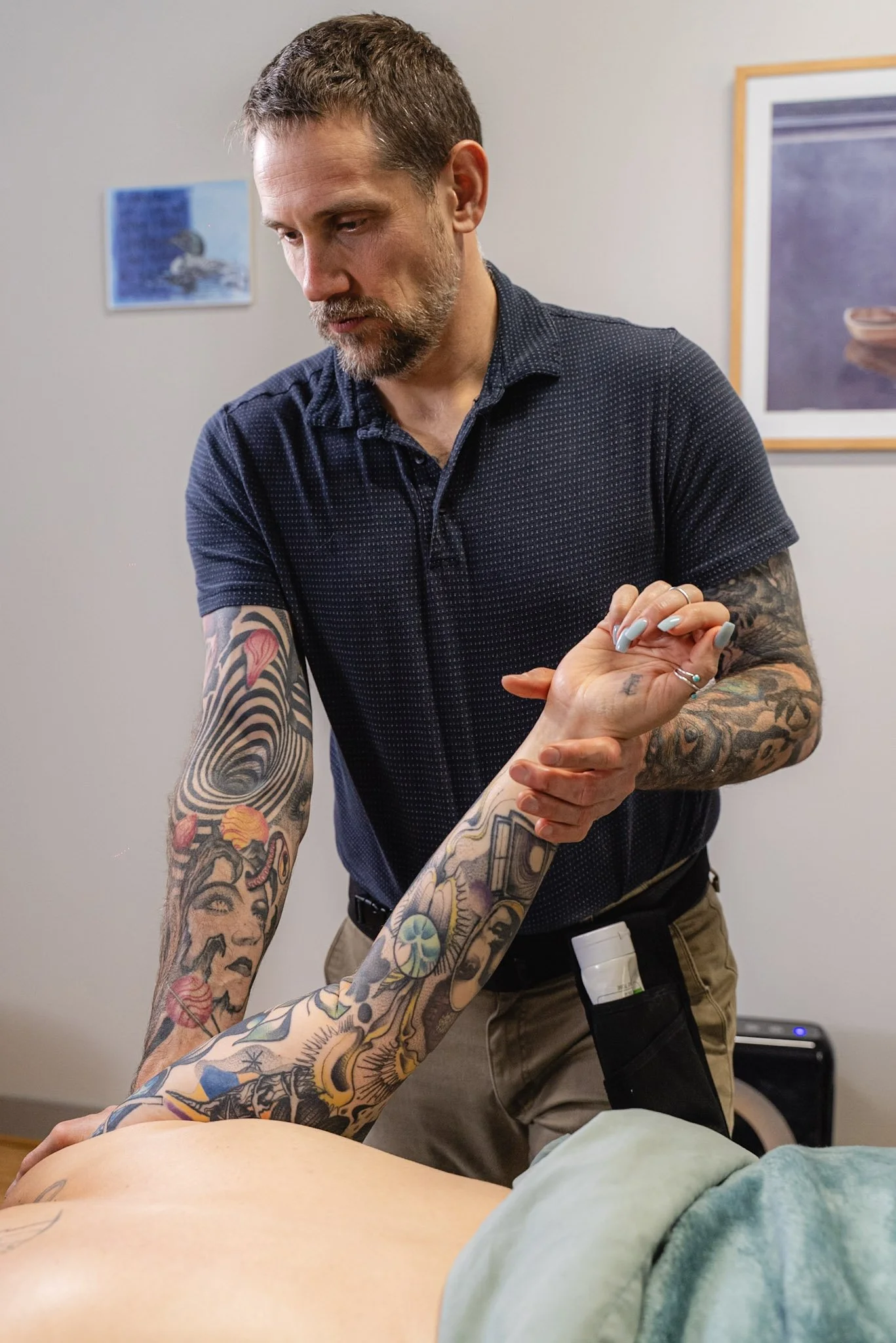 Therapist with tattoos stretches backward right arm of tattooed female client