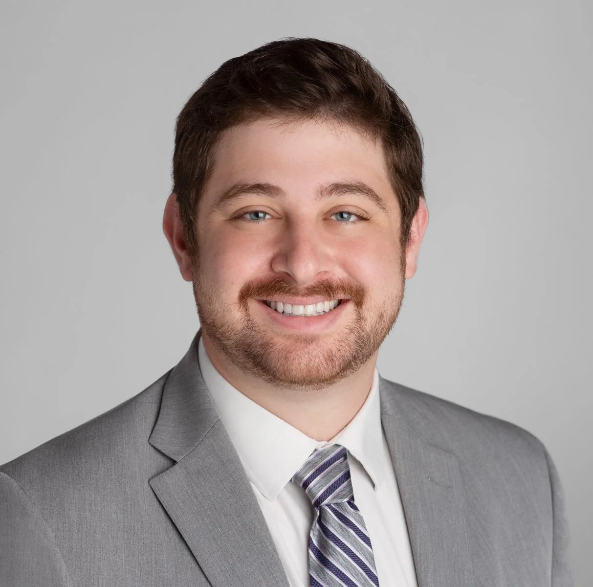 photo of a white man with a beard wearing a grey suit and tie