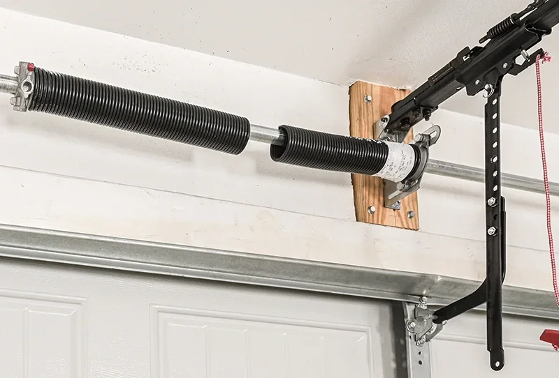 Garage door torsion spring mounted above the garage door, connected to a metal torsion rod and a hanging garage door opener arm.