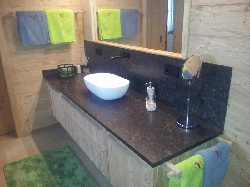 Ein Badezimmer mit Waschbecken, Spiegel, schwarzen Arbeitsplatte, Handtüchern und Dekorationsgegenständen.