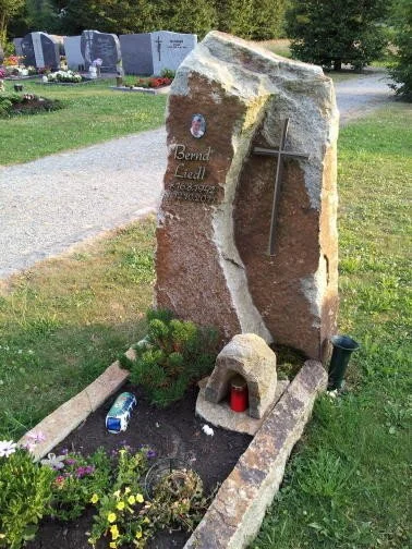Grabstein mit Kreuz im Friedhof, Blumen und Kerzen davor