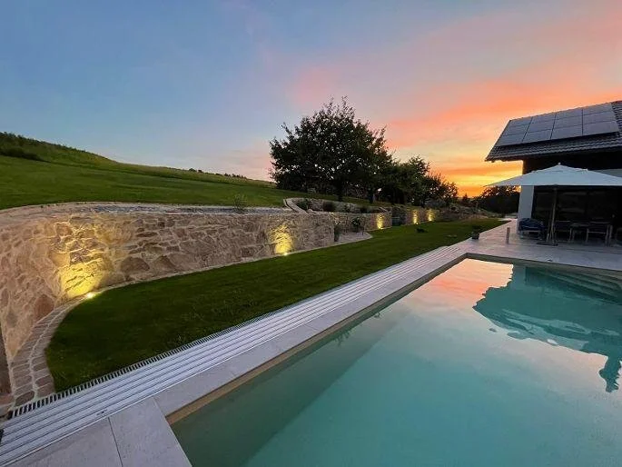 Trockenmauer aus regionalem Naturstein als elegante Gartenmauer. Witterungsbeständige Konstruktion mit LED Beleuchtung neben Pool und Terrasse. Perfekte Außengestaltung für Mauern, Grenzen und Landschaftsbereiche.