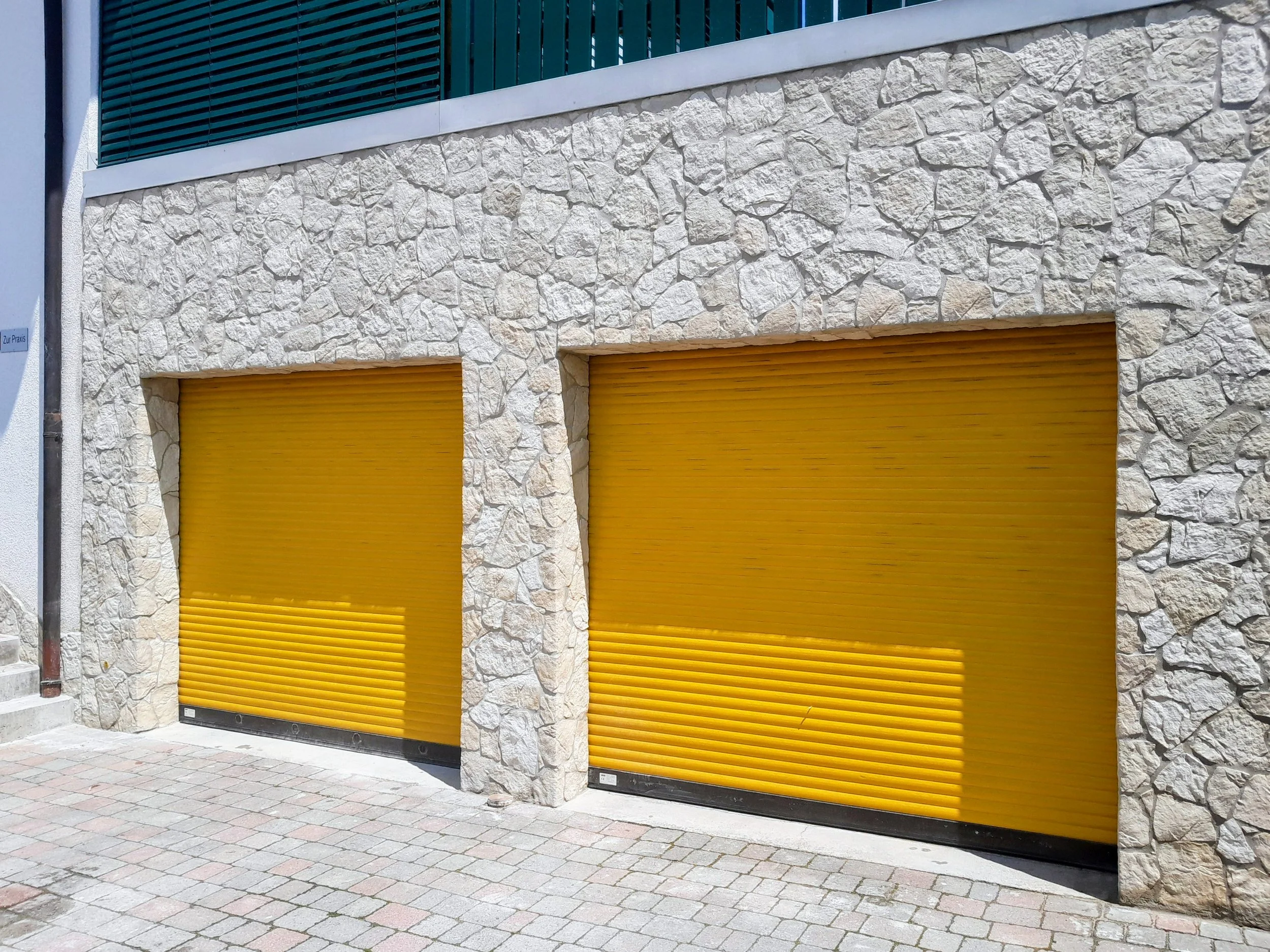Zwei gelbe Rolltore vor einer Steinwand an einer modernen Gebäudefassade.