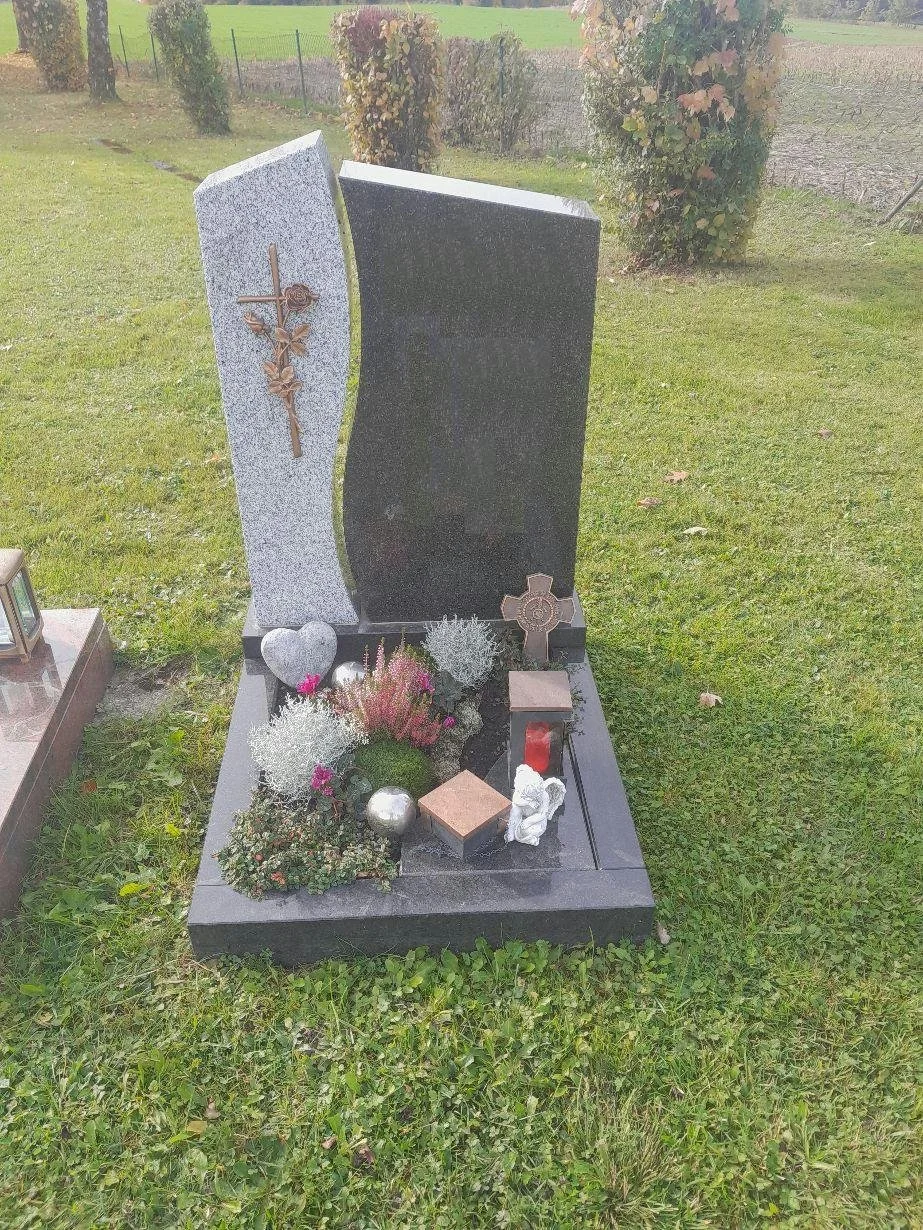 Ein Grabstein mit einer schwarzen Seite, eine metallene Rose und Kreuze, Blumen und Dekorationen im Garten