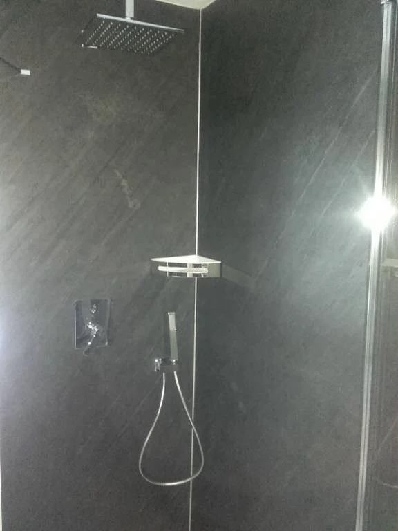 Dusche mit dunklen Fliesen, Regenbrausekopf, Handbrause und Ablage.